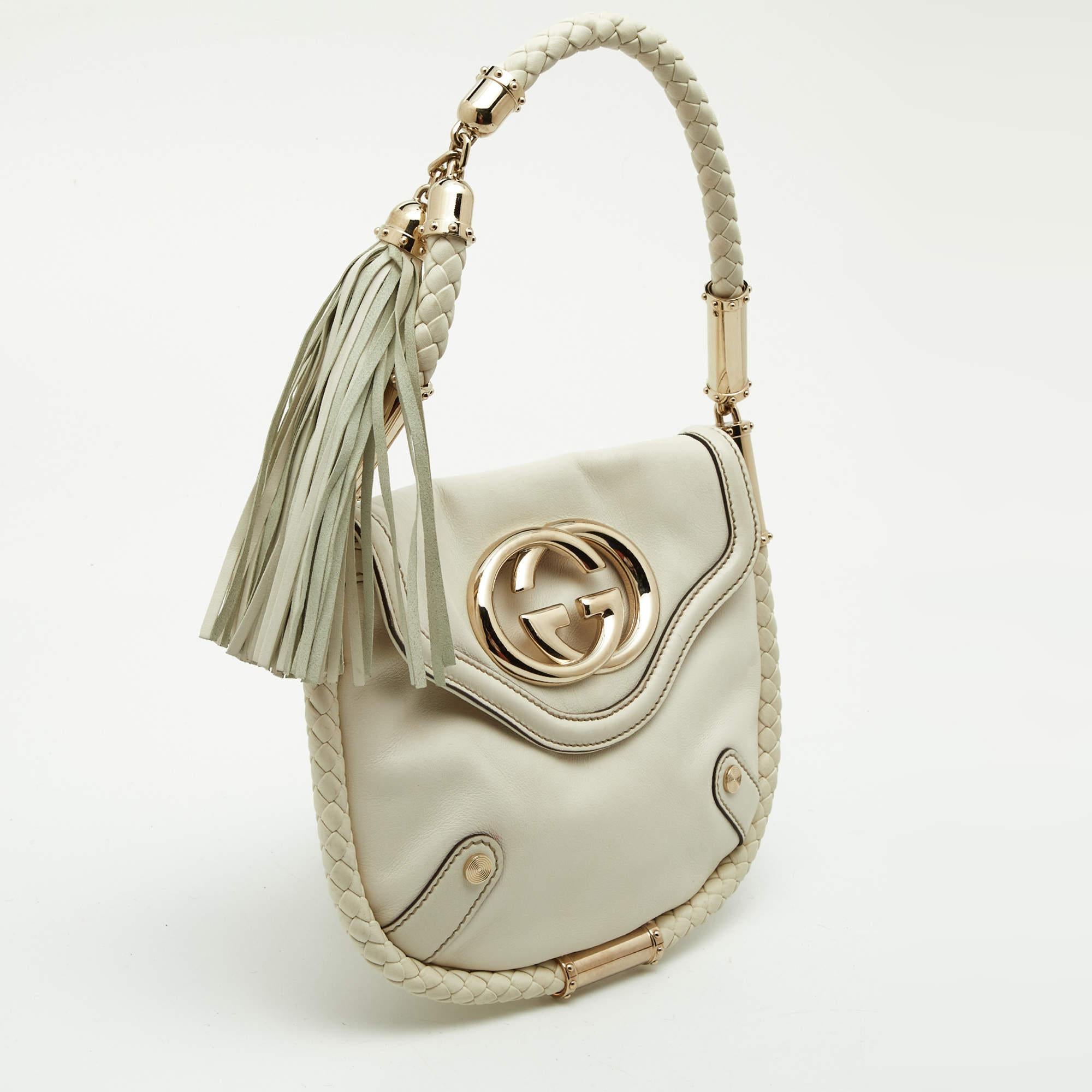 This Gucci shoulder bag looks classy because of the off-white leather and braided rolled handle with tassels. The interior compartment is lined with fabric and gold-toned GG logo on the flap top with snap closure.


