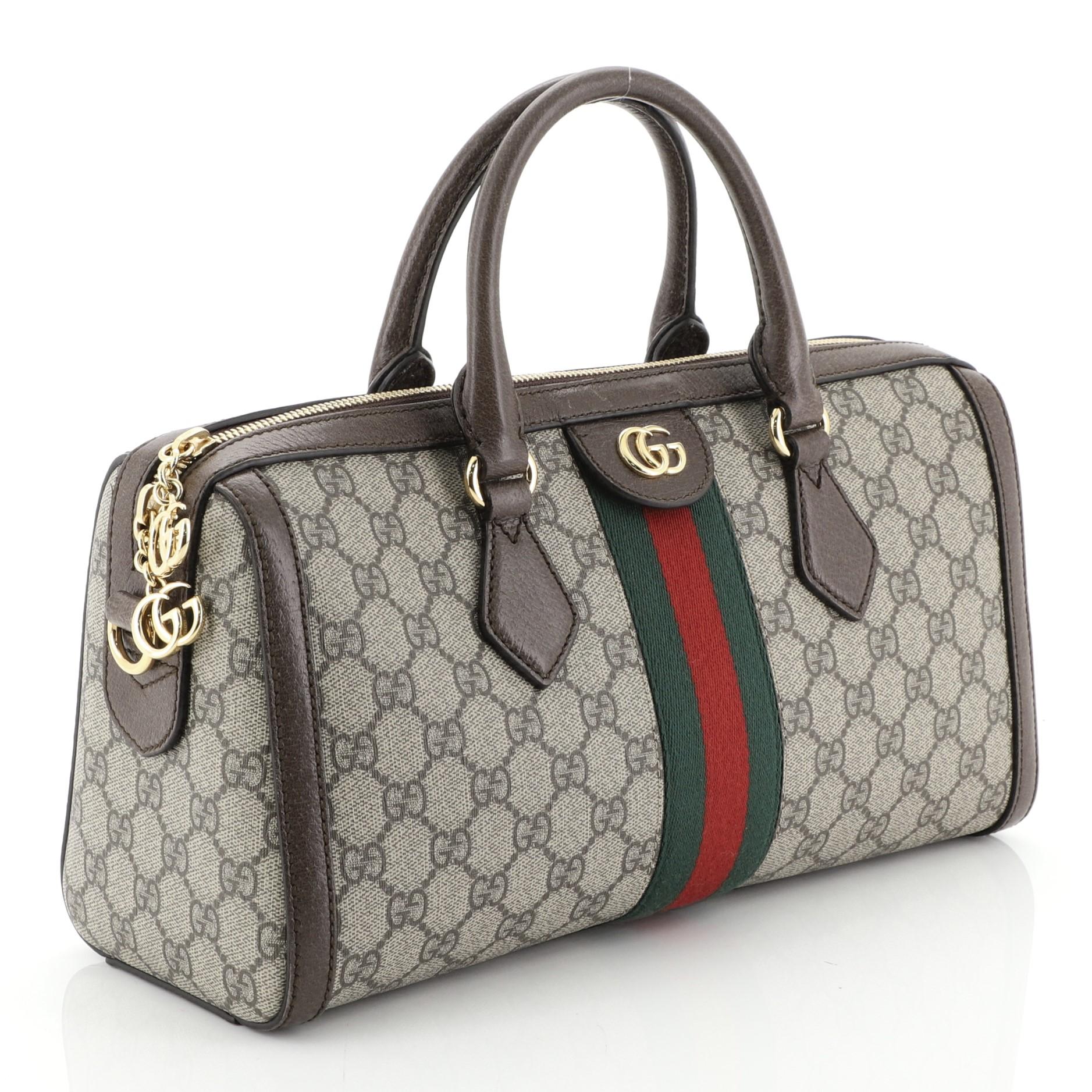 This Gucci Ophidia Boston Bag GG Coated Canvas Medium, crafted in brown GG coated canvas, features dual rolled leather handles, leather trim, web stripe detail, and gold-tone hardware. Its zip closure opens to a neutral microfiber interior.