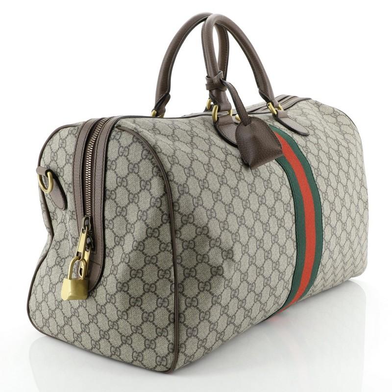 This Gucci Ophidia Carry On Duffle Bag GG Coated Canvas Large, crafted in brown GG coated canvas, features inlaid web stripe detail, dual rolled leather handles, leather trim, and gold-tone hardware. Its zip closure opens to a neutral fabric