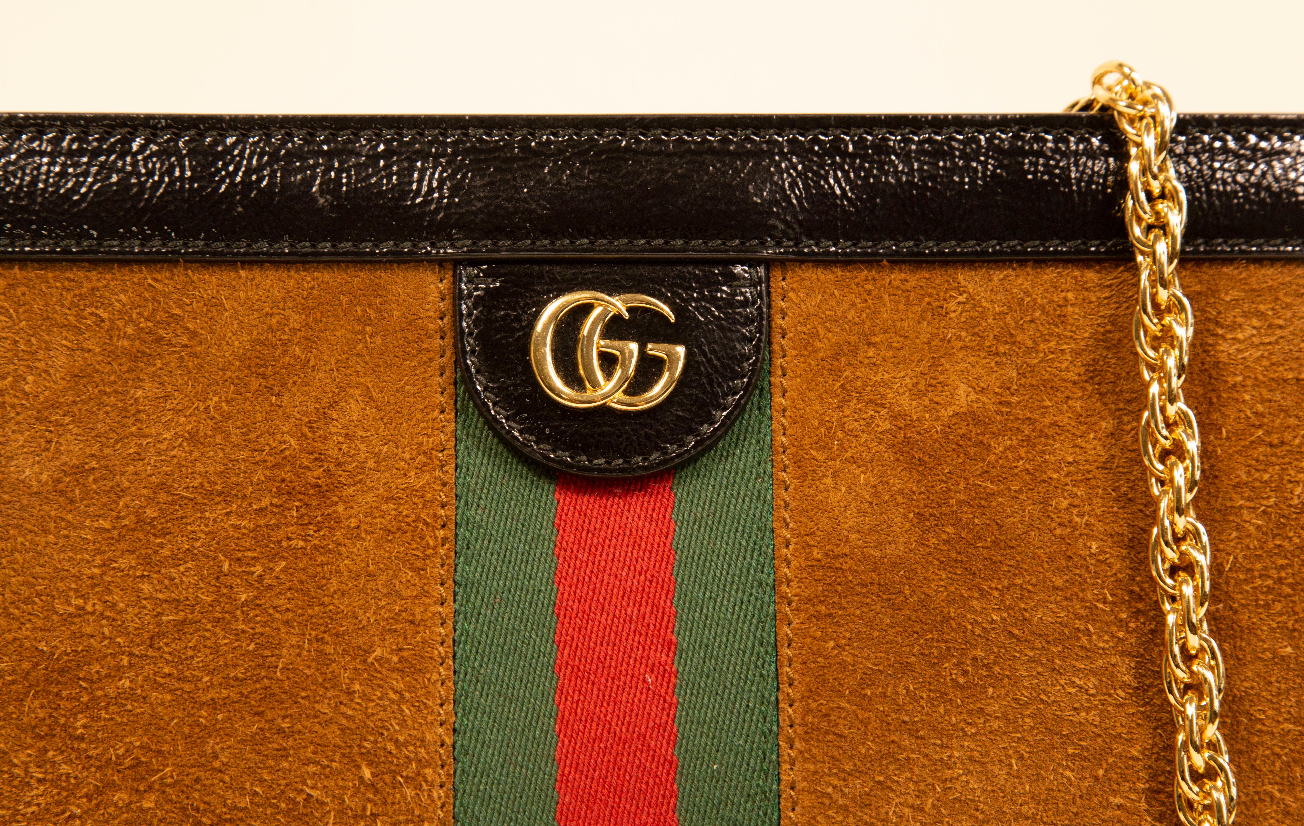 A Gucci Ophidia Chain shoulder bag made of cognac brown suede with black patent leather trim and gold tone hardware. The interior is lined with blue silky fabric. The inner compartment is divided into two compartments of which one features one slide