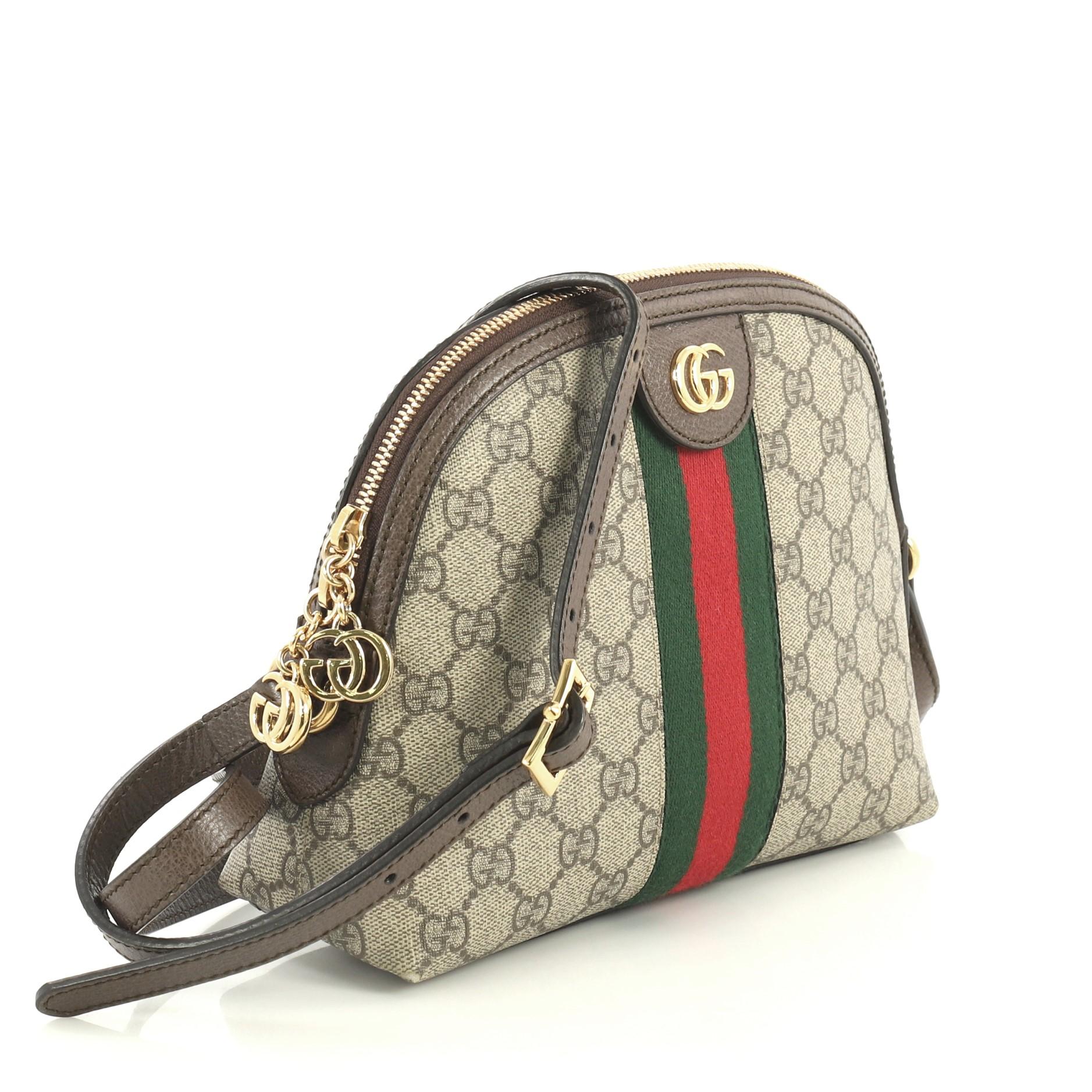 This Gucci Ophidia Dome Shoulder Bag GG Coated Canvas Small, crafted in brown GG coated canvas, features an adjustable leather strap, web striped design, and gold-tone hardware. Its zip closure opens to a blue satin interior with slip pockets.