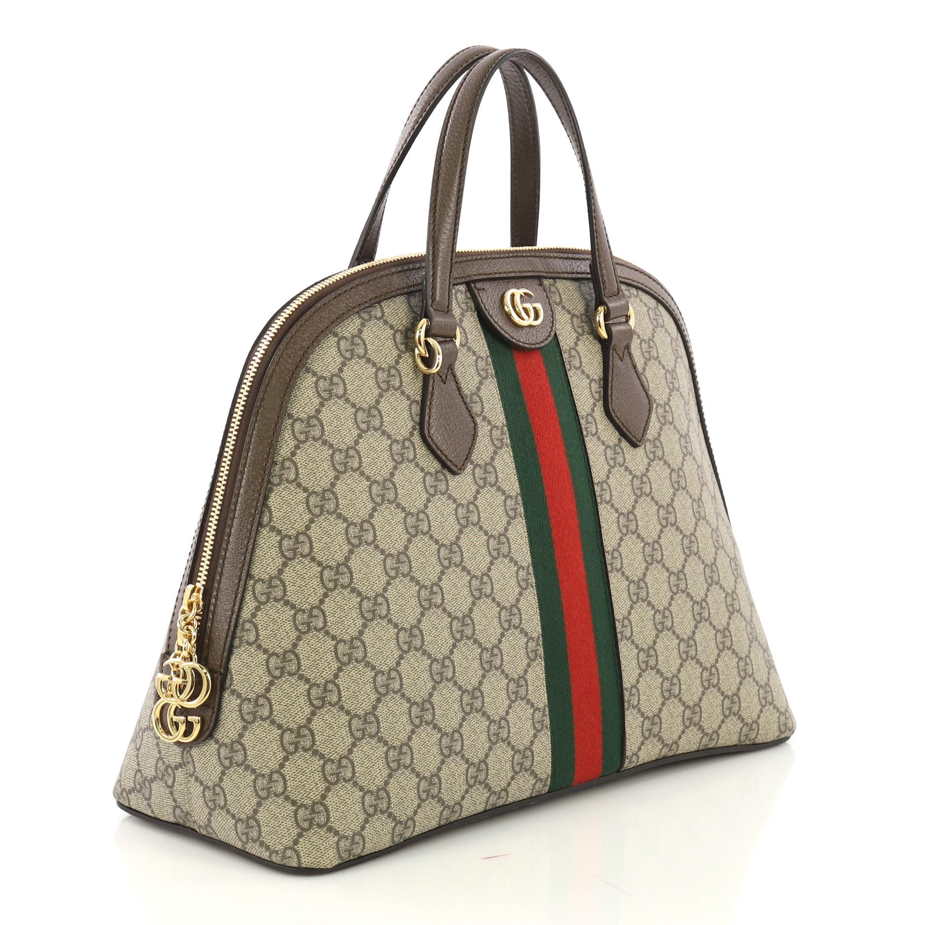 This Gucci Ophidia Dome Top Handle Bag GG Coated Canvas Medium, crafted in brown GG coated canvas, features dual leather handles, web stripe detail, and gold-tone hardware. Its zip closure opens to a nude microfiber interior with side zip and slip