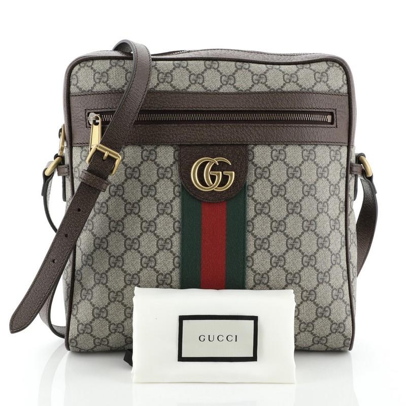 This Gucci Ophidia Messenger Bag GG Coated Canvas Medium, crafted in brown GG coated canvas, features an adjustable leather strap, web striped design, exterior front zip pocket, and aged gold-tone hardware. Its zip closure opens to a neutral fabric