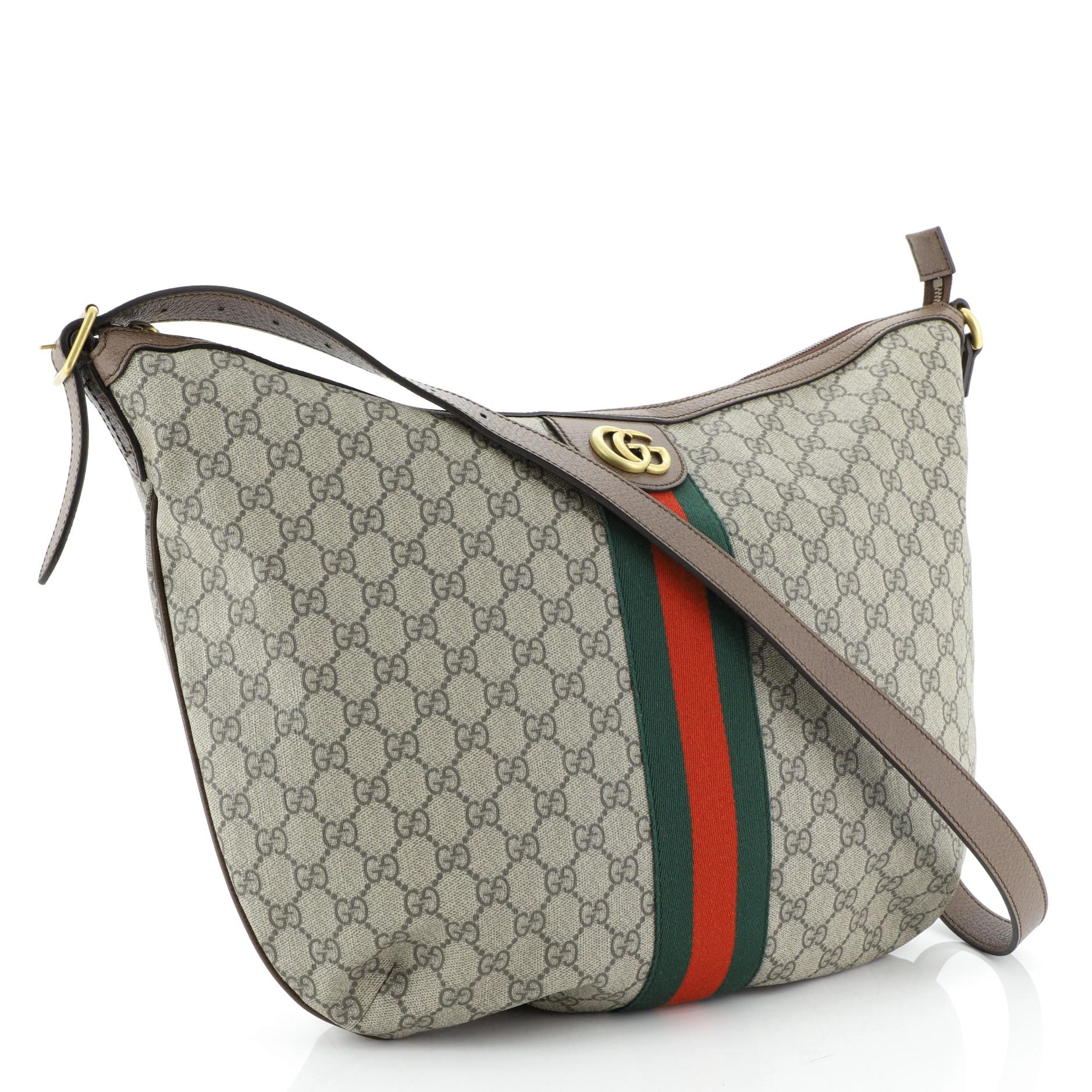 This Gucci Ophidia Shoulder Bag GG Coated Canvas, crafted in brown GG coated canvas, features an adjustable leather strap, web striped design, and brass-tone hardware. Its zip closure opens to a neutral fabric interior with side zip and slip