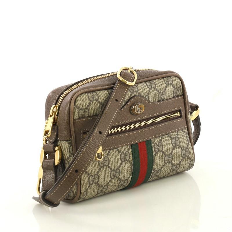 This Gucci Ophidia Shoulder Bag GG Coated Canvas Mini, crafted in brown GG coated canvas, features an adjustable leather strap, web stripe design, exterior front zip pocket, and gold-tone hardware. Its top zip closure opens to a neutral microfiber