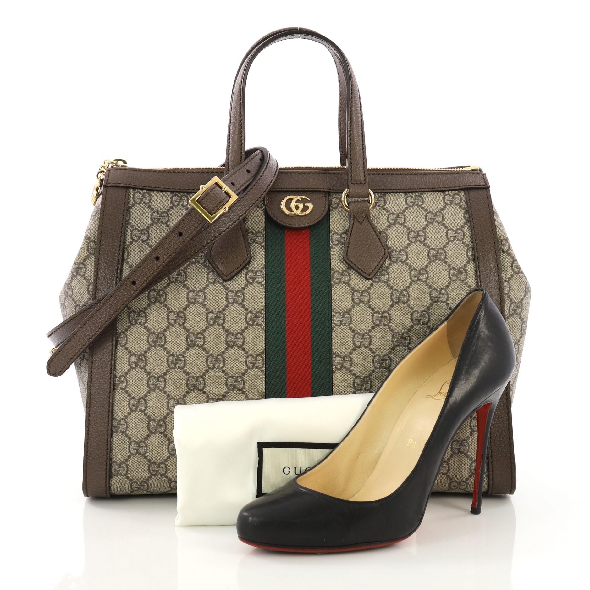 This Gucci Ophidia Top Handle Bag GG Coated Canvas Medium, crafted in brown GG supreme coated canvas, features dual flat handles, web strap detailing, and gold-tone hardware. Its zip closure opens to a pink microfiber interior with zip and slip
