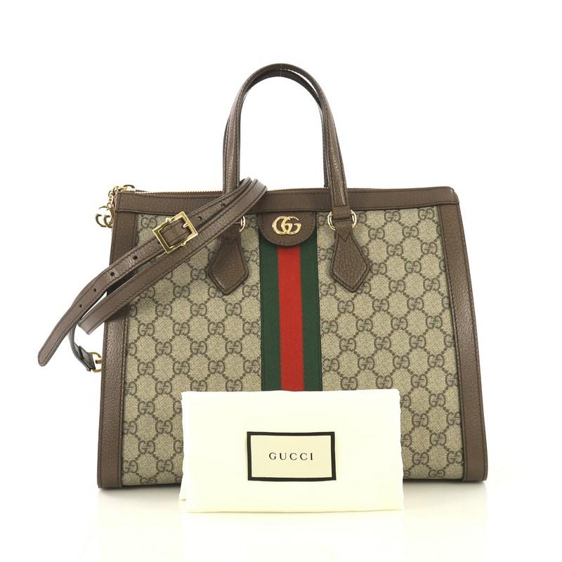 This Gucci Ophidia Top Handle Bag GG Coated Canvas Medium, crafted in brown GG supreme coated canvas, features dual flat handles, web strap detailing, leather trim, and gold-tone hardware. Its zip closure opens to a neutral microfiber interior with
