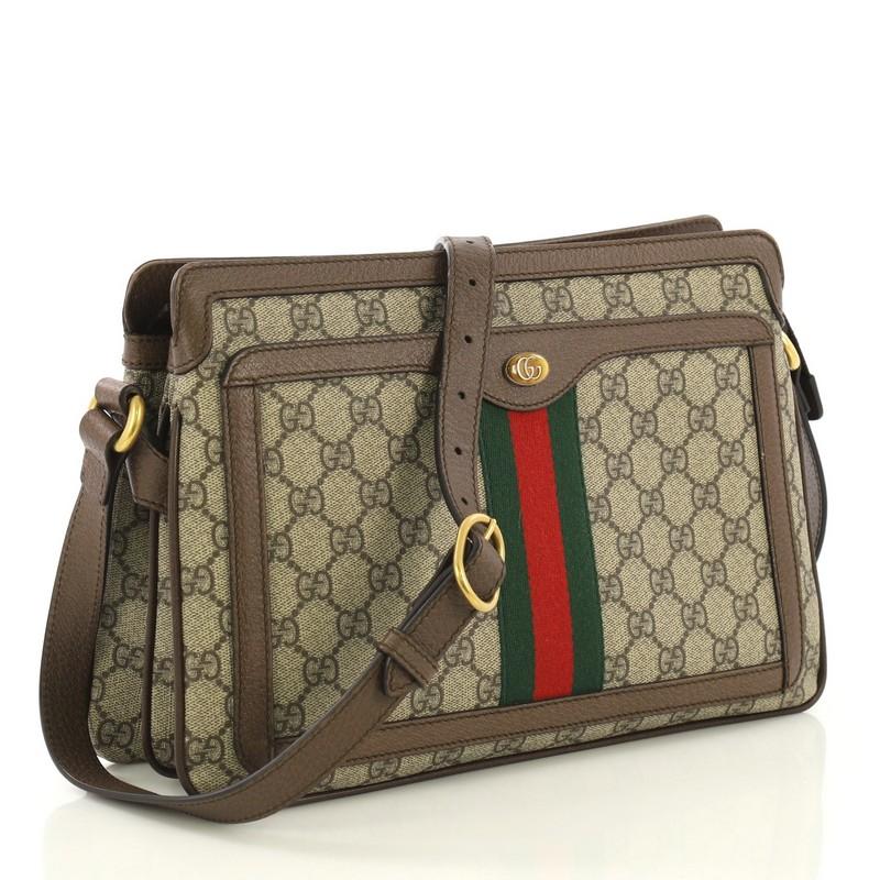 This Gucci Ophidia Zip Shoulder Bag GG Coated Canvas Medium, crafted in brown GG coated canvas, features an adjustable leather strap, web striped design, exterior front pocket, and aged gold-tone hardware. Its zip closure opens to a beige fabric