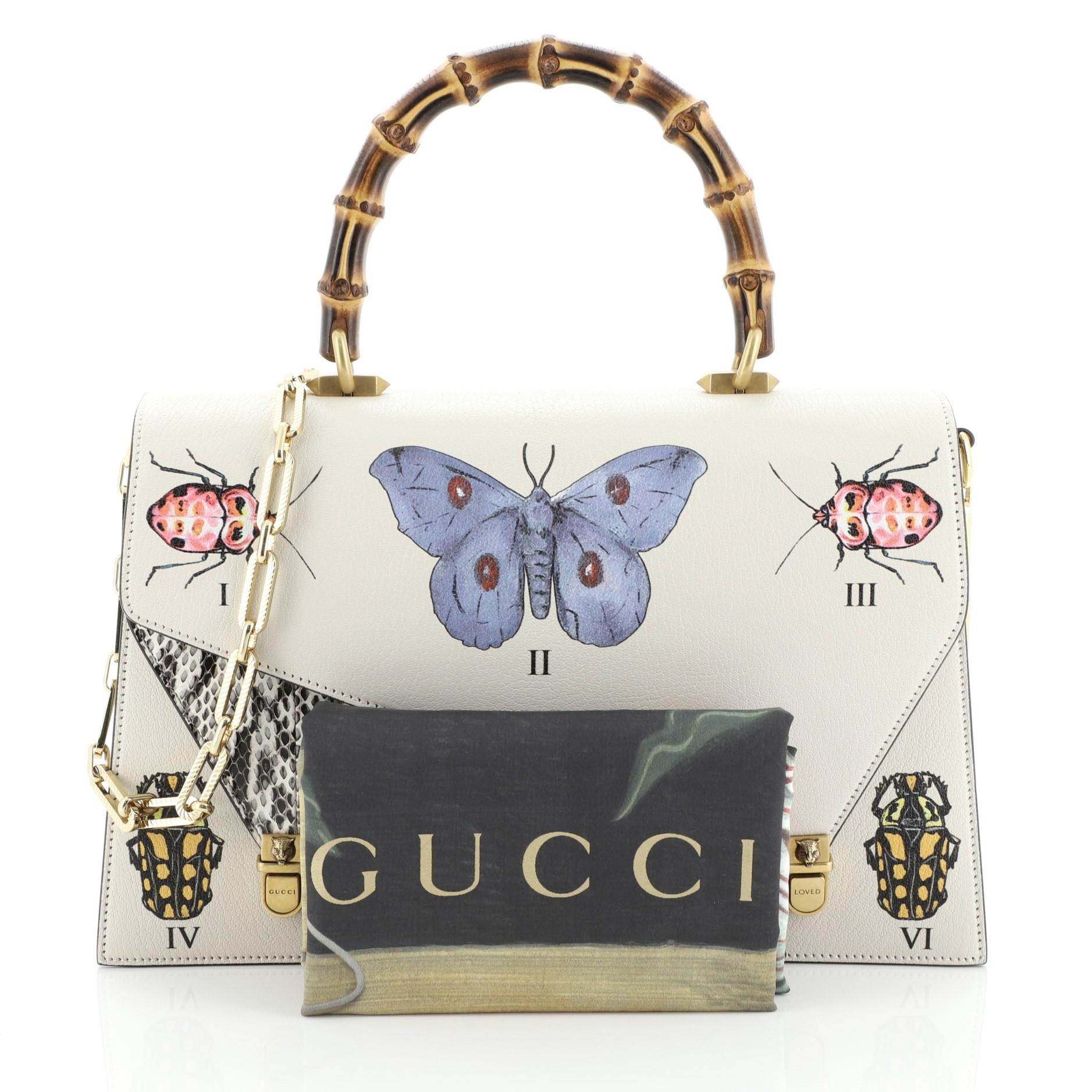 This Gucci Ottilia Top Handle Bag Painted Leather with Snakeskin Medium, crafted in multicolor printed and neutral leather, features a bamboo top handle, overlapping double flap, hand-painted butterflies and insect and aged gold-tone hardware. Its