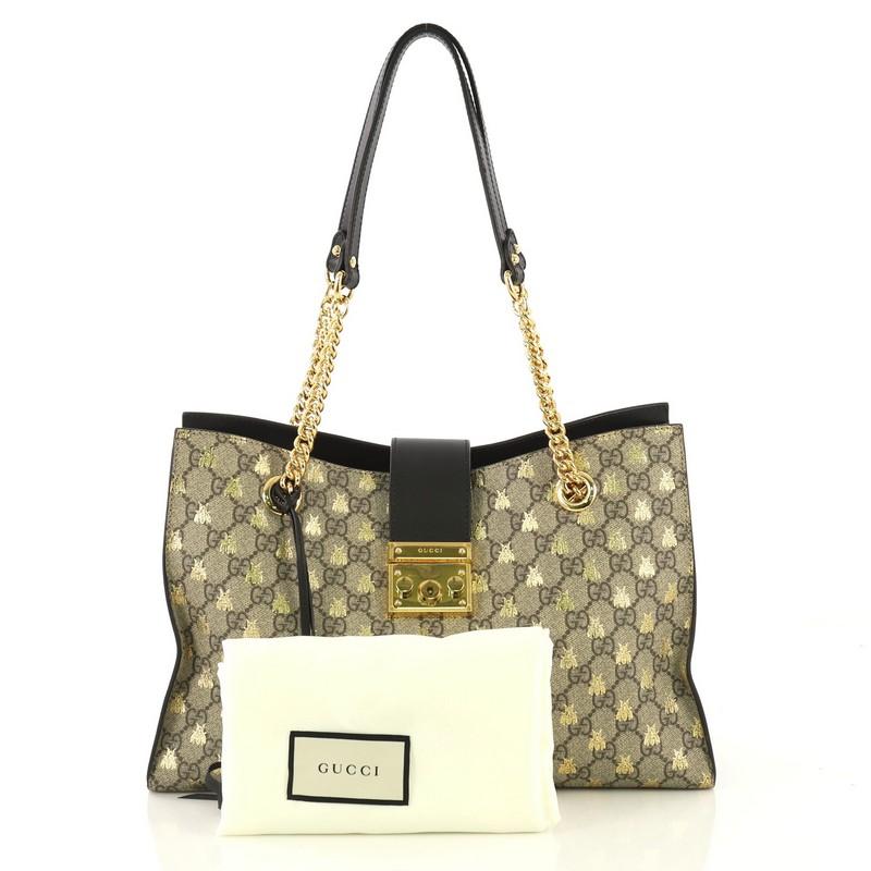 This Gucci Padlock Chain Tote Printed GG Coated Canvas Medium, crafted in neutral GG coated canvas and black leather, features dual chain link straps with leather pads and gold-tone hardware. Its padlock tab closure opens to a neutral microfiber