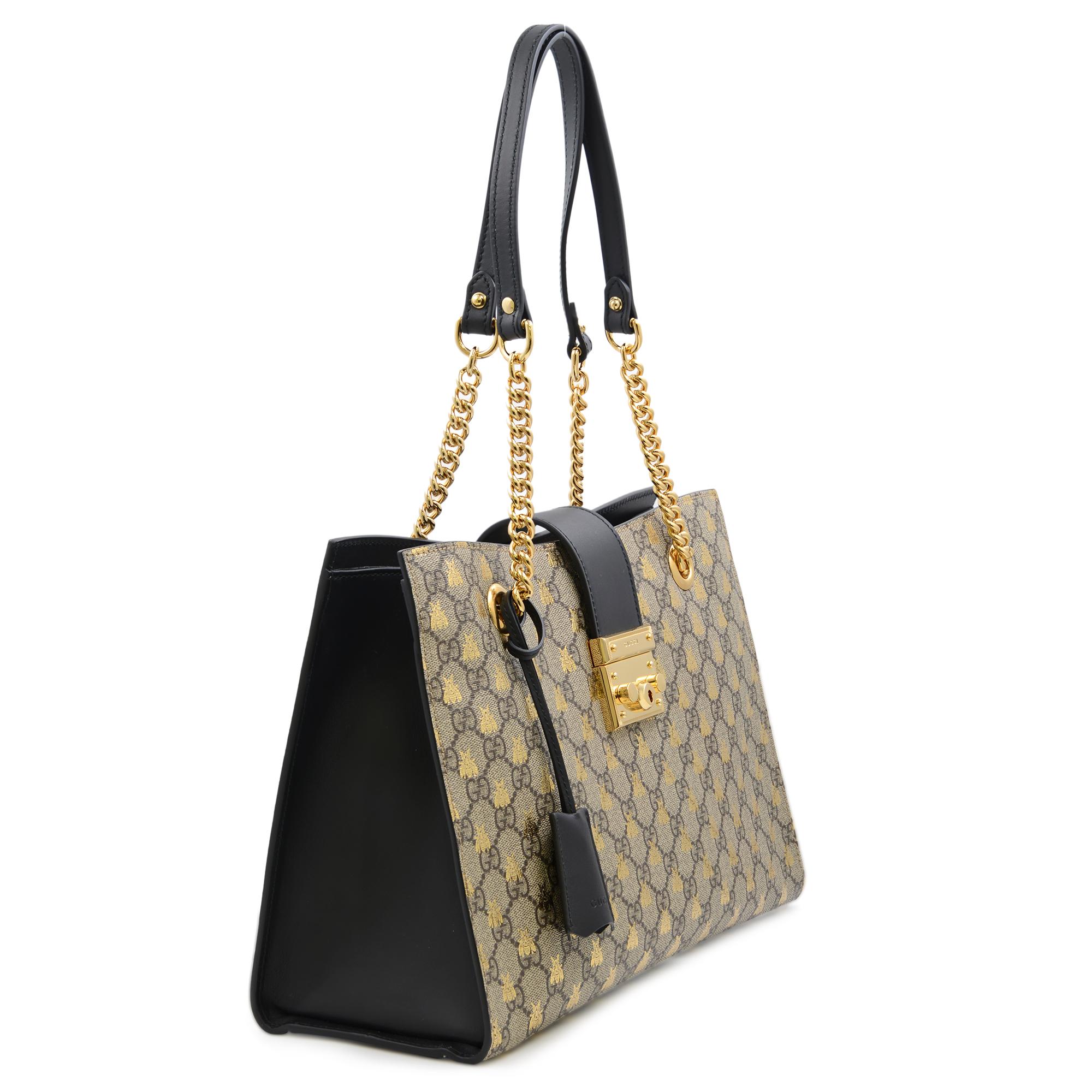 A structured shoulder bag by Gucci in GG Supreme gold Bee print with leather and chain shoulder straps; 9.5 inches drop. Open top with flap-over padlock closure. Gold-tone hardware. Key with hanging leather holder. Interior two open and one zip