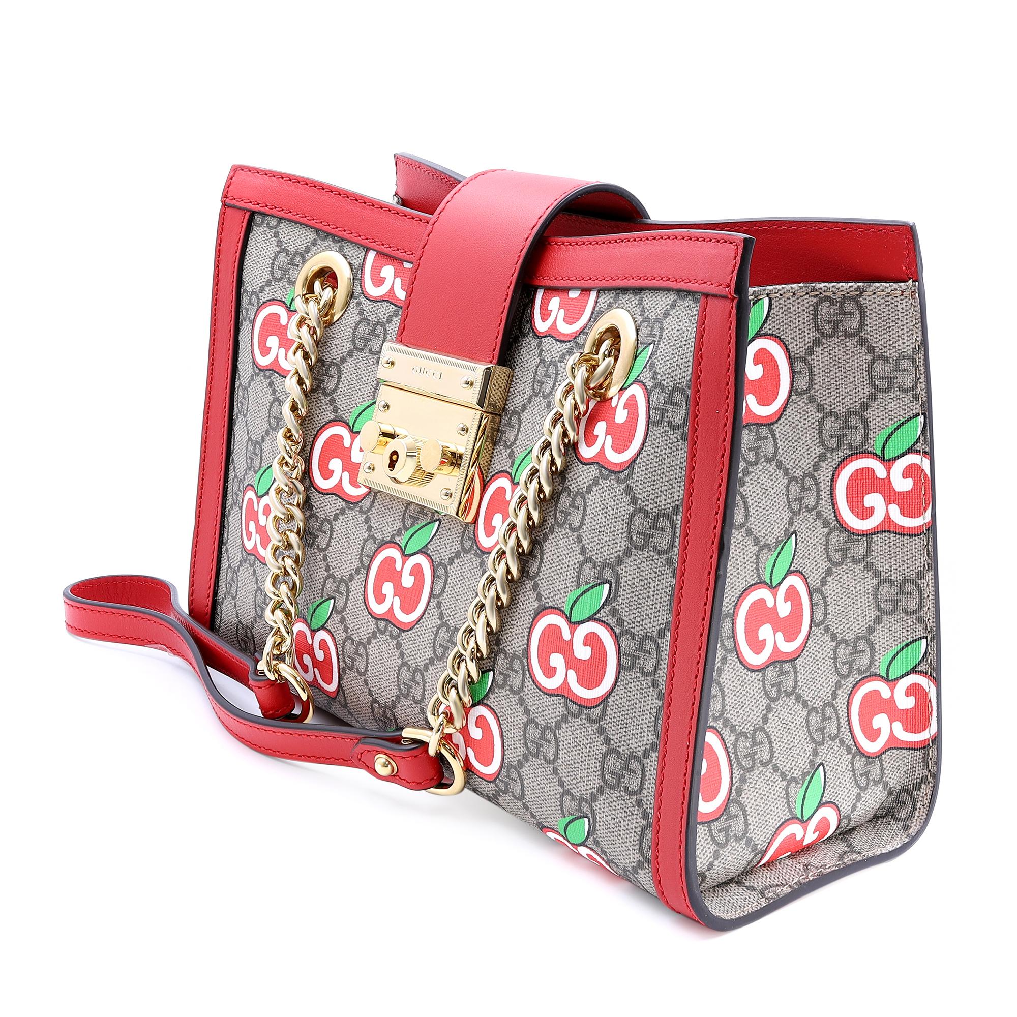 Gucci Padlock small shoulder bag featuring apple print GG supreme canvas with red leather trim. Comes with a half chain and half leather shoulder straps. Push snap flap closure. The top opens to a beige microfiber lining with two interior patch