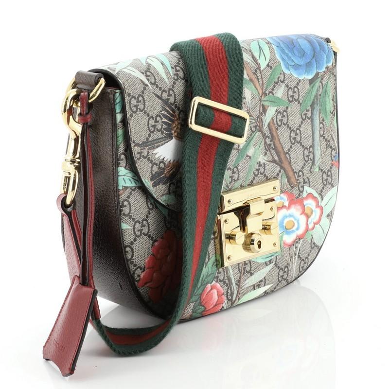 This Gucci Padlock Saddle Shoulder Bag Tian Print GG Coated Canvas Medium, crafted from brown GG coated canvas with Tian print, features an adjustable web strap and gold-tone hardware. Its push-lock closure opens to a neutral microfiber interior