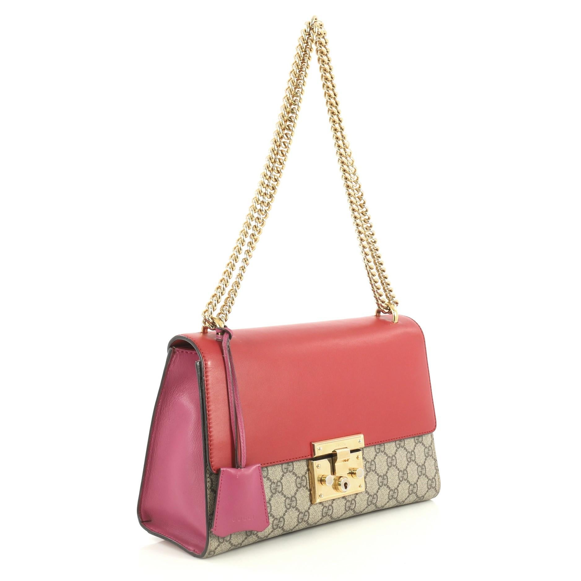 This Gucci Padlock Shoulder Bag GG Coated Canvas and Leather Medium, crafted in brown GG coated canvas and red leather, features chain link strap, exterior back slip pocket, and gold-tone hardware. Its push-lock closure opens to a brown microfiber