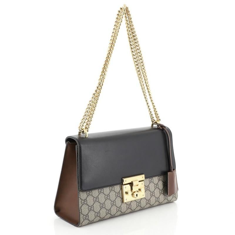 This Gucci Padlock Shoulder Bag GG Coated Canvas and Leather Medium, crafted in brown GG coated canvas and black leather, features chain link strap, exterior back slip pocket, and gold-tone hardware. Its push-lock closure opens to a brown microfiber