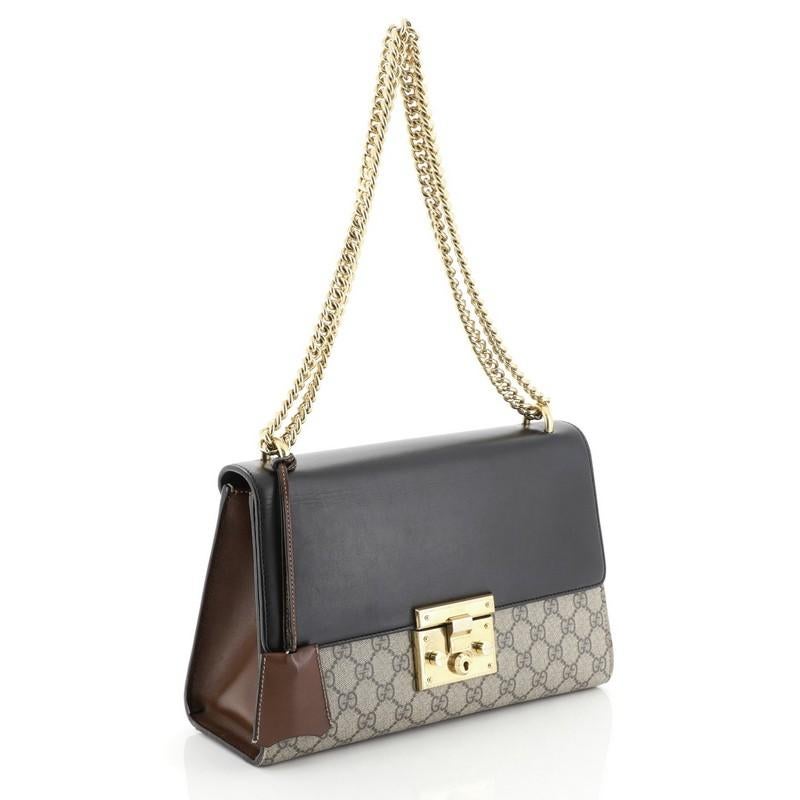 This Gucci Padlock Shoulder Bag GG Coated Canvas and Leather Medium, crafted in brown GG coated canvas and black leather, features chain link strap, exterior back slip pocket, and gold-tone hardware. Its push-lock closure opens to a brown microfiber