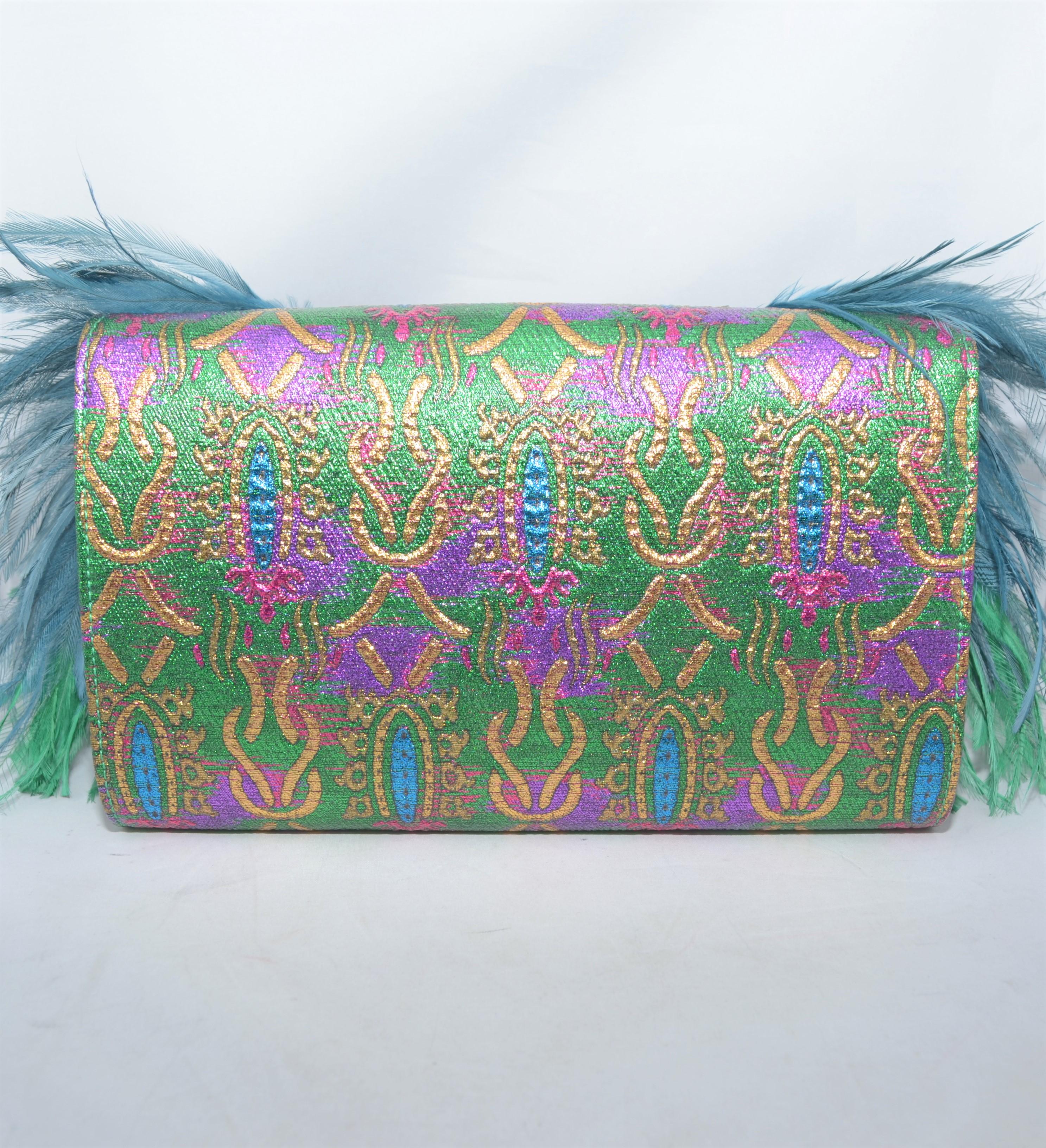 Gucci clutch is featured in a blue/green iridescent color on brocade with rhinestone embellishing that creates the image of a peacock, and feathers that adorn the sides of the clutch. Fully lined clutch with an optional brass-tone chain handle.