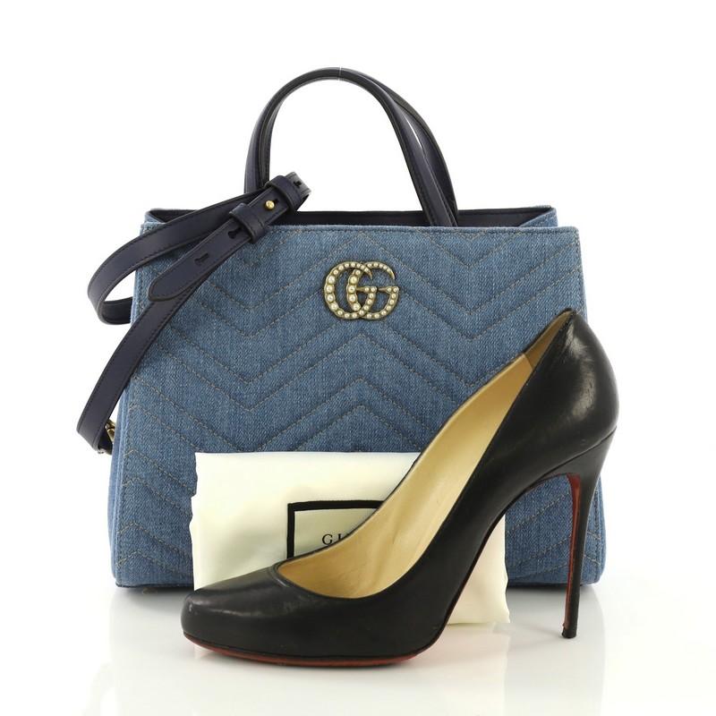 This Gucci Pearly GG Marmont Tote Matelasse Denim Small, crafted from blue matelasse denim, features dual top leather handles, interlocking pearl studded GG logo, protective based studs, and aged gold-tone hardware. Its magnetic snap closure opens