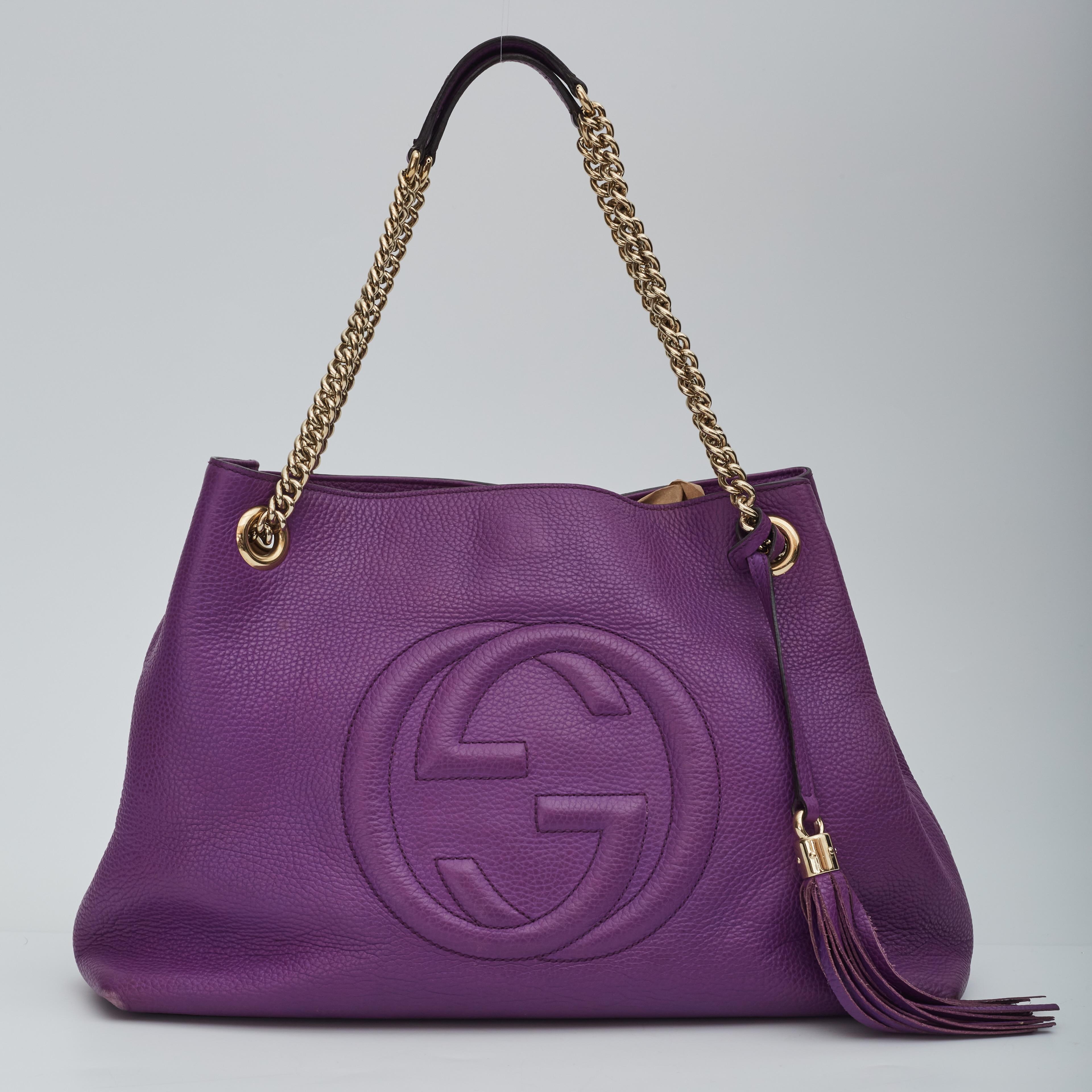 This shoulder bag is made of textured calfskin leather in purple. The bag features a prominent front interlocking GG quilted logo, polished light gold chain link shoulder straps with shoulder pads and a decorative light gold knobbed tassel. The top