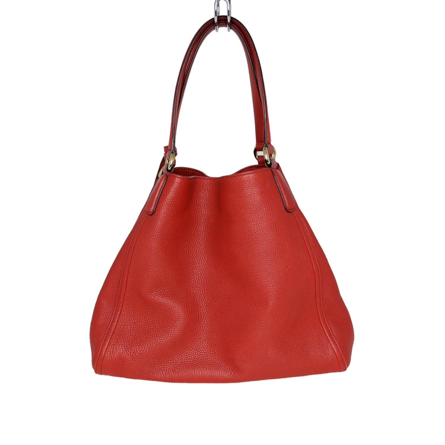 This stylish medium sized tote is crafted of finely textured calfskin leather in red with a quilted interlocking G logo on the front. The handbag features leather strap handles with polished brass links, an open top with ban clasp, and a beige
