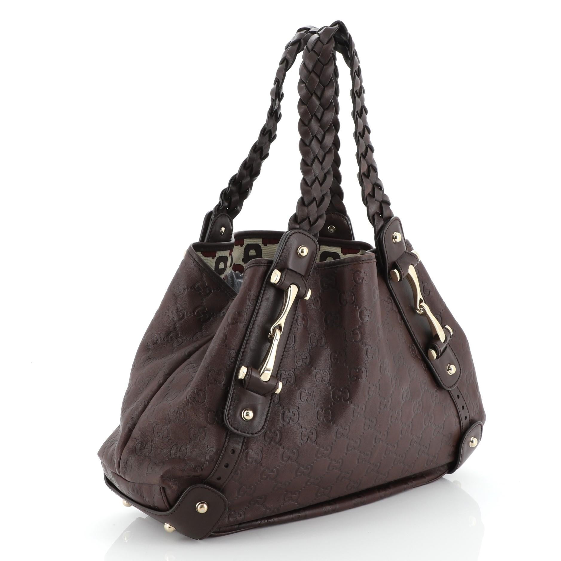 This Gucci Pelham Shoulder Bag Guccissima Leather Small, crafted in brown guccissima leather, features braided leather straps, signature horsebit detailing, and gold-tone hardware. Its wide top opening showcases a neutral printed fabric interior