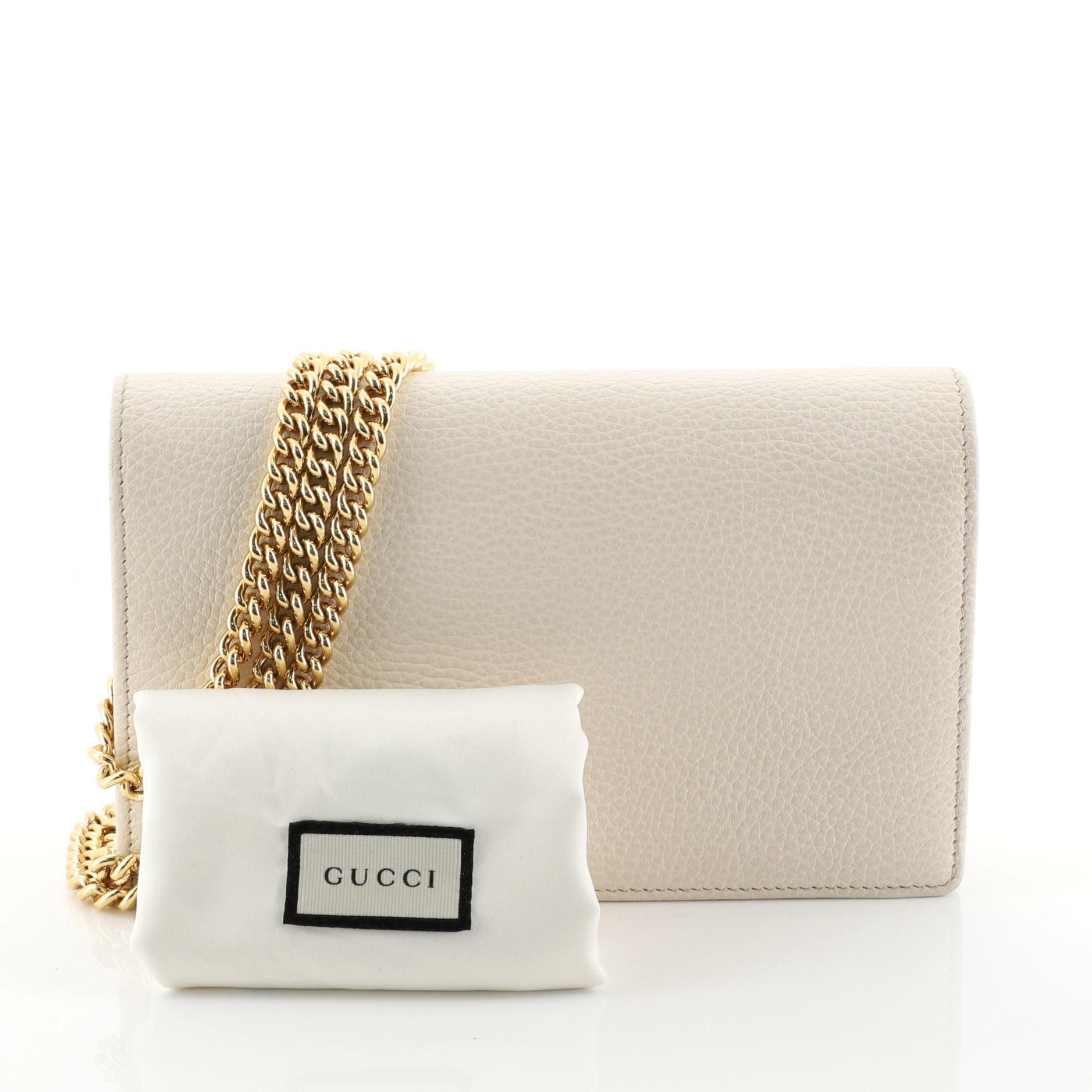 This Gucci Petite GG Marmont Chain Wallet Leather Mini, crafted from white leather, features chain link strap, double G logo at front flap, and gold-tone hardware. Its snap button closure opens to a black fabric and white leather interior with
