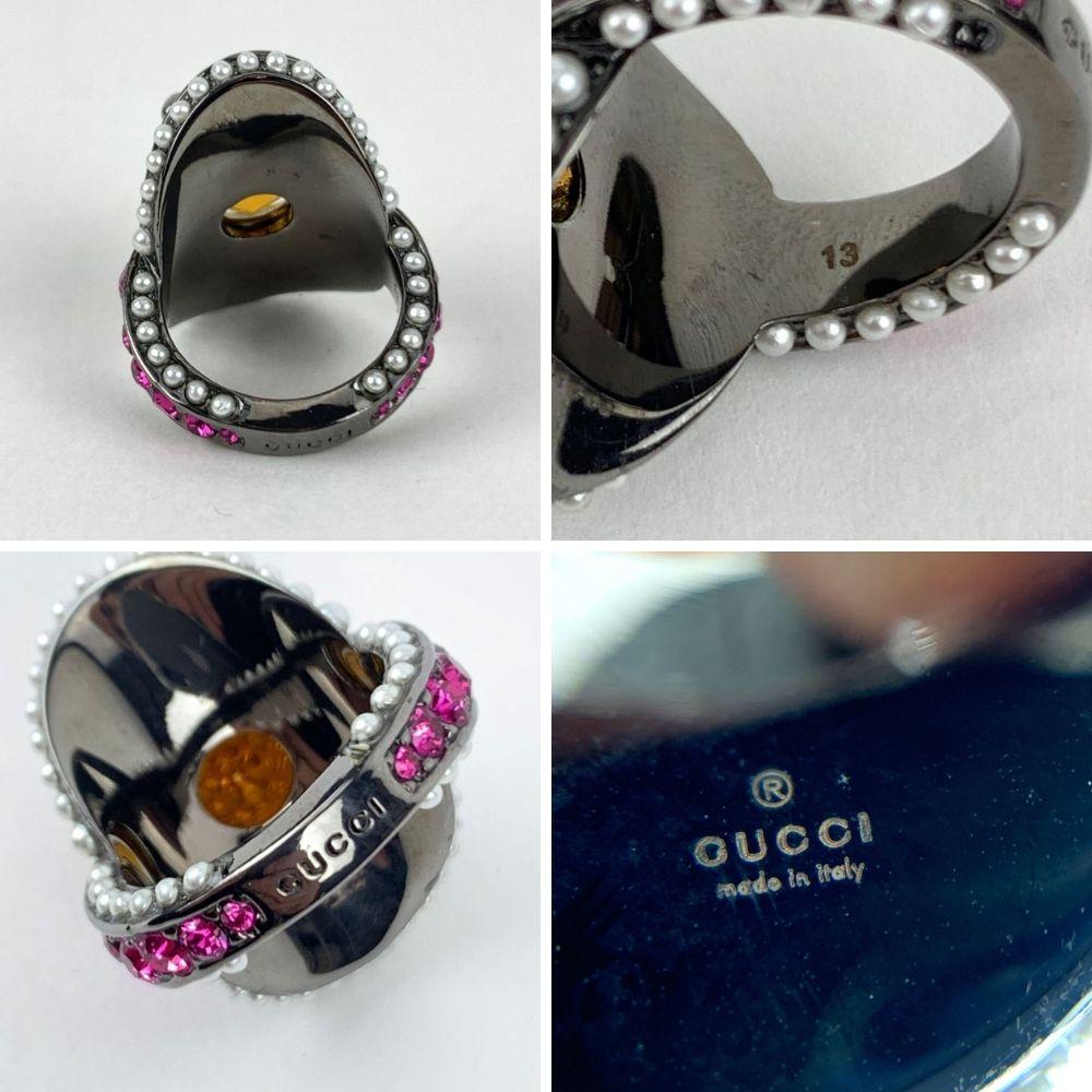 Beautiful embellished 'Spike' ring by Gucci. It features a gunmetal body, embellished with small pink crystals and a large yellow crystal with a gold metal spike on top. Small white pearls detailing along the edges. Size: 13 IT (it should correspond