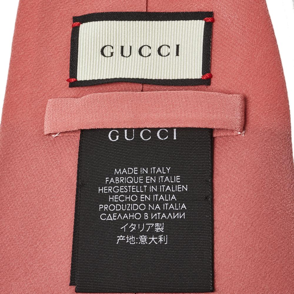 Diese markante Gucci-Krawatte ist aus Seide gefertigt und hat einen breiten Schnitt mit einer 12 cm langen Spitze. Der rosafarbene Hintergrund wird von drei gestickten Ananas kontrastiert:: was den lebendigen Ton fortsetzt. Sie ist mit einer