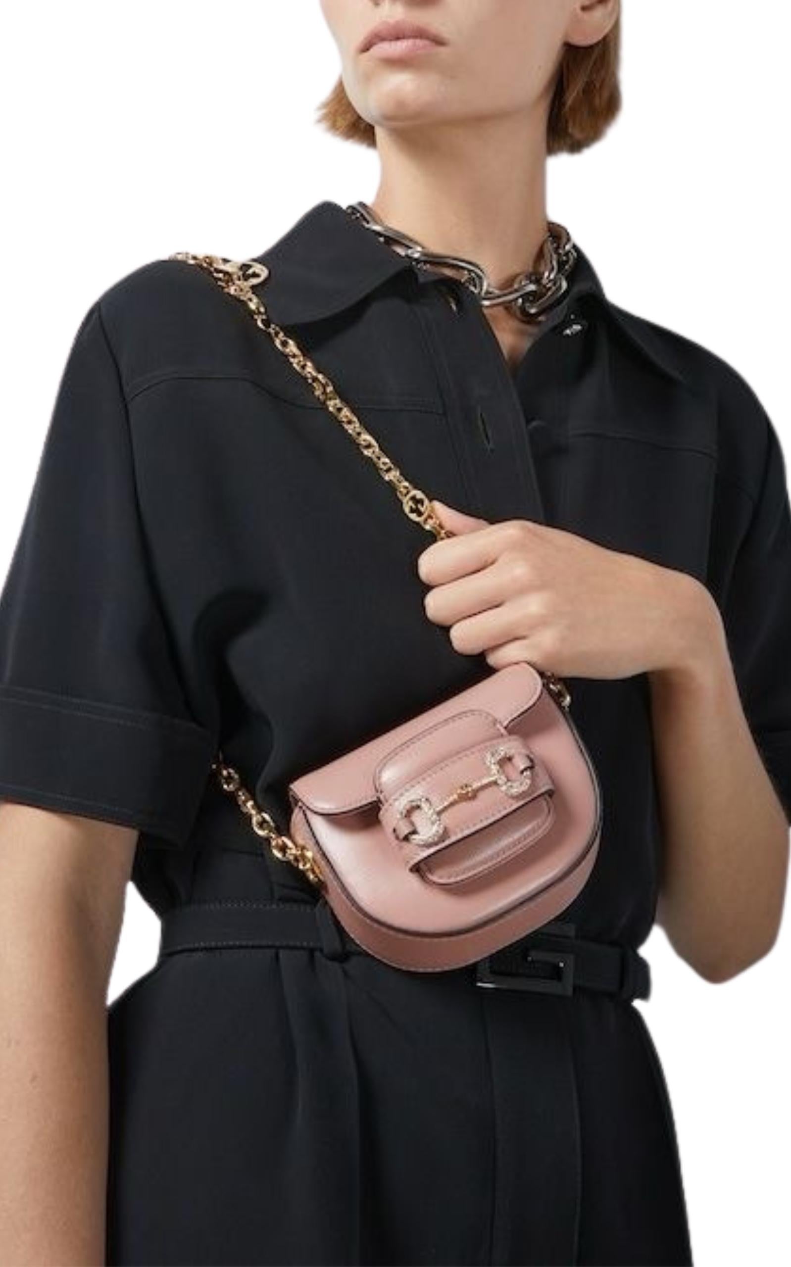 Pink ‘Horsebit 1955’ belt bag from Gucci. Made from calf leather, this design secures via a sliding fastener and showcases the brand's signature horsebit plaque encrusted with sparkling crystals on the front, gold-tone metal hardware as well as a