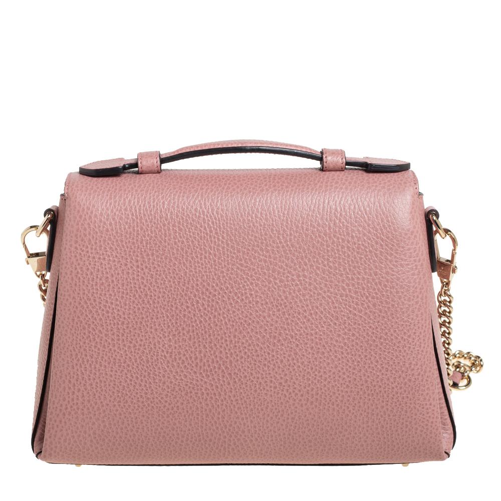 This Gucci top handle bag is a minimal design that exhibits sophistication. Crafted from pink leather, it features a structured silhouette adorned with a logo accented front flap that opens to a well-sized interior. Hold it by the top handle and