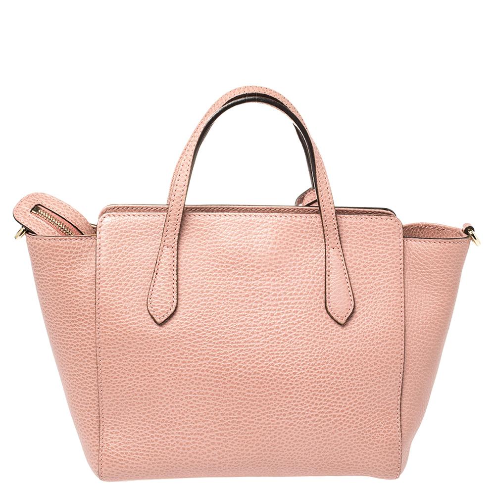 This chic and trendy Swing tote by Gucci exudes brilliance and outstanding craftsmanship. Crafted from leather in a pink hue, it has a structured shape adorned by the label's logo. The zipper closure opens to a well-sized interior for your