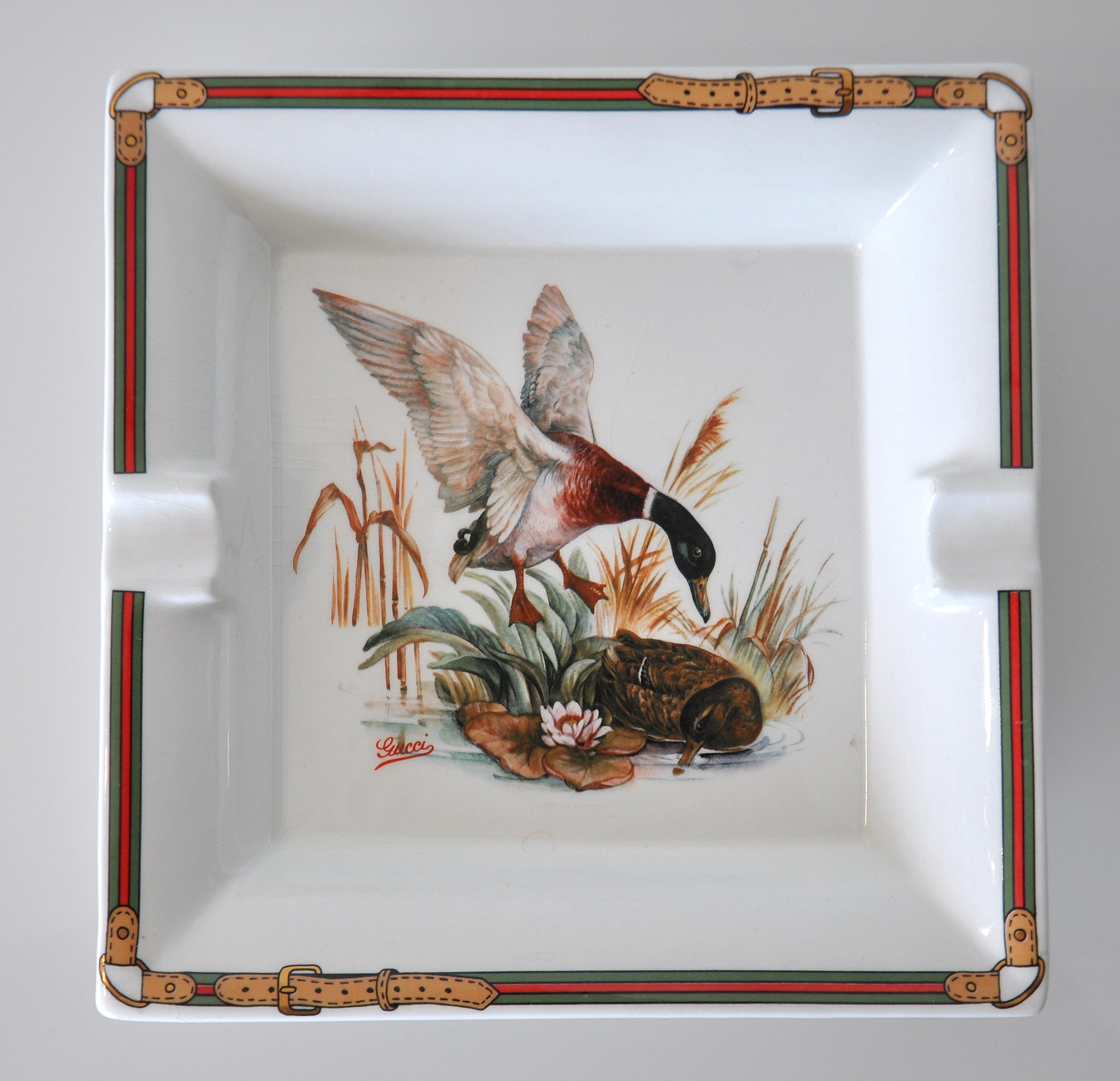 Fine porcelain cigar ashtray by Gucci with classic hunting motif depicting a pair of exquisitely detailed mallard ducks near a pond with iconic Gucci striped belt border decorations and intricate details. The ashtray can also be used as a small tray