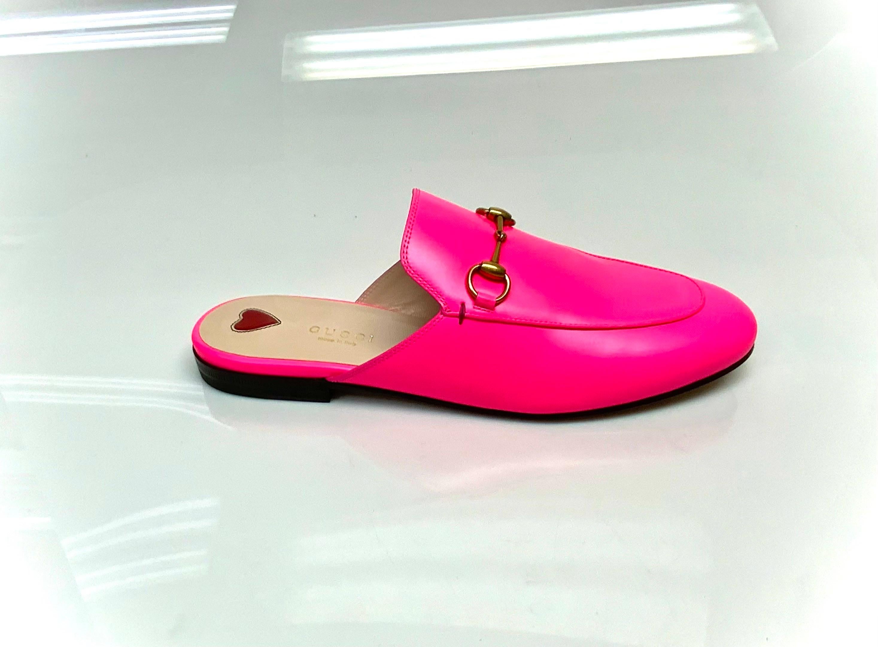 These chic loafers are crafted of smooth neon pink calfskin leather. They feature an aged gold horse bit embellishment, a rounded toe, and a 0.5 inch heel. The Gucci princetown slides will be staple in anyone's closet. This item is NEW and NEVER