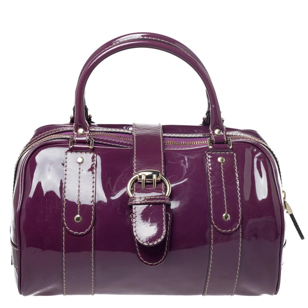 Crafted from purple patent leather, this Gucci number has bow detailed buckled flap on the exterior along with a logo-engraved metal plaque at the front, two handles, and studs in gold-tone hardware. It comes with a spacious fabric interior. Flaunt