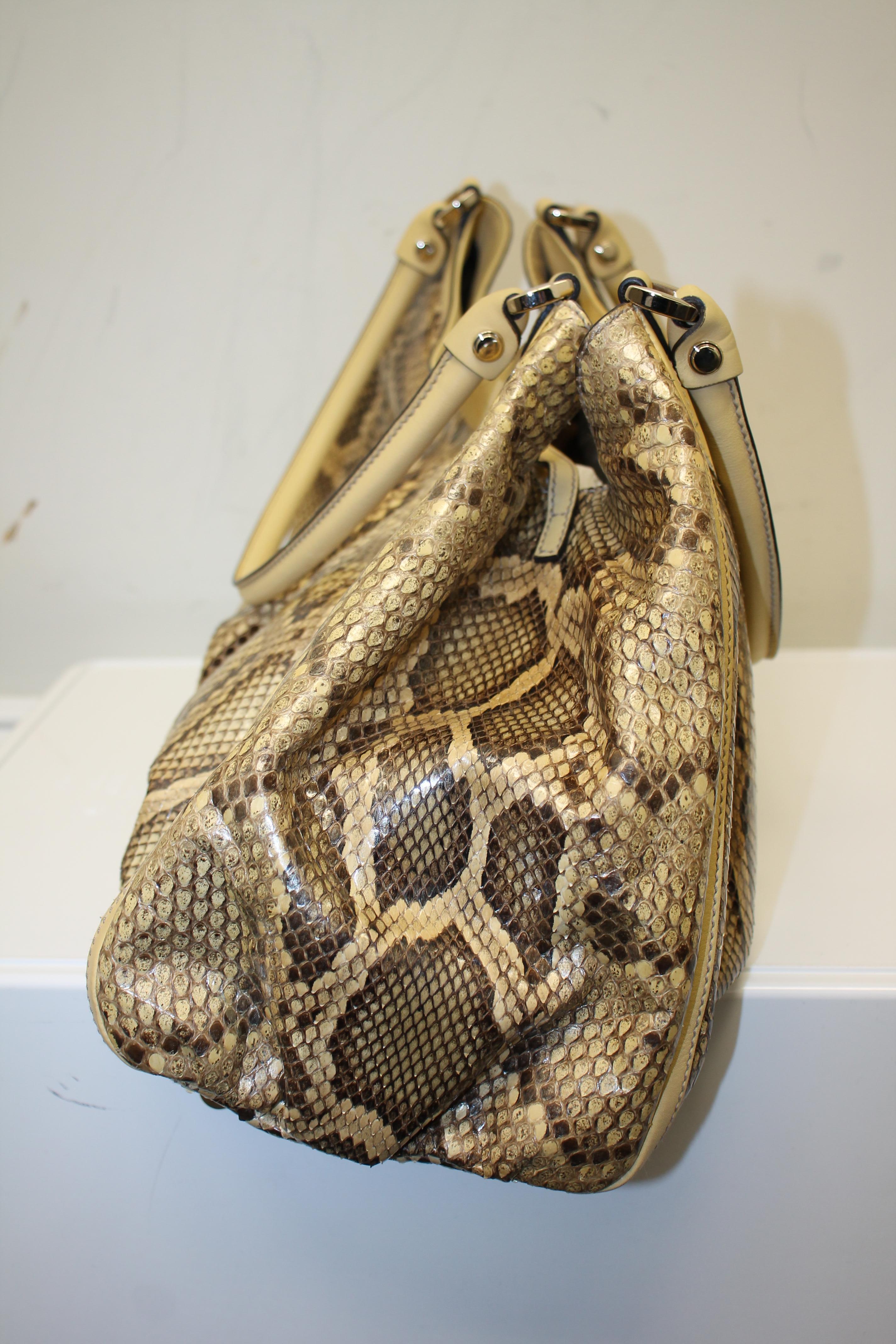 Tan and brown tone python. Silver-tone hardware. Beige leather trim. Clip lock closure at top. Dual leather top rolled handles. Protective feet at base. Lined interior. One interior opened phone pocket. One interior zippered pocket.