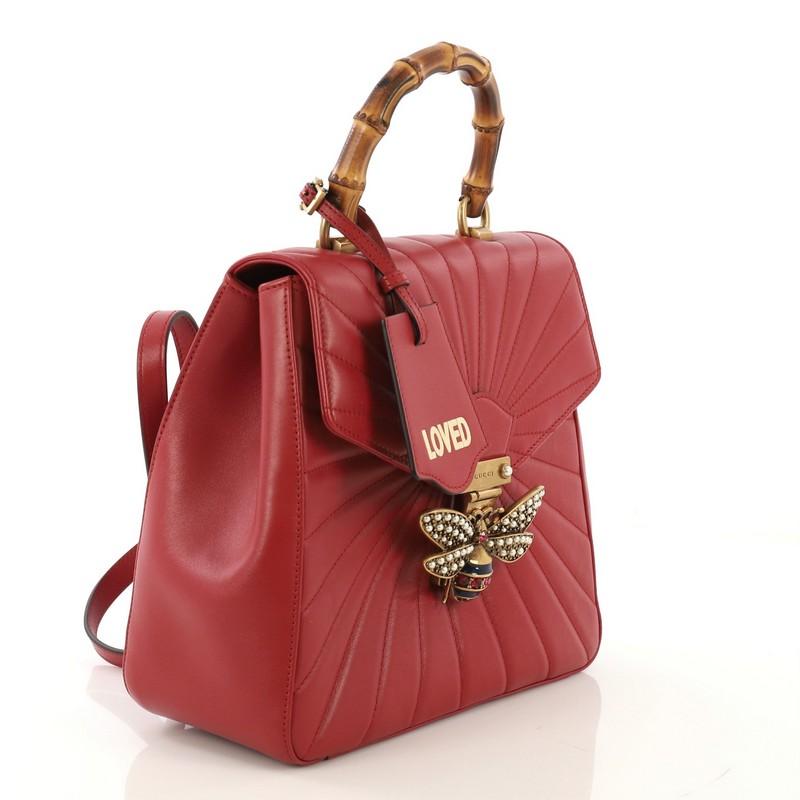 This Gucci Queen Margaret Backpack Quilted Leather Small, crafted from red quilted leather, features a bamboo top handle, adjustable backpack straps, bejeweled bee on its flap, and aged gold-tone hardware. It opens to a light pink microfiber