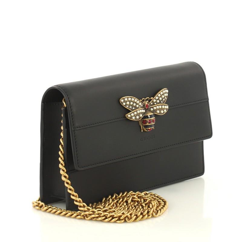 This Gucci Queen Margaret Chain Wallet Leather Mini, crafted from black leather, features bejeweled bee on its flap, slip pocket under flap, and aged gold-tone hardware. Its snap button closure opens to a black fabric and leather interior with zip
