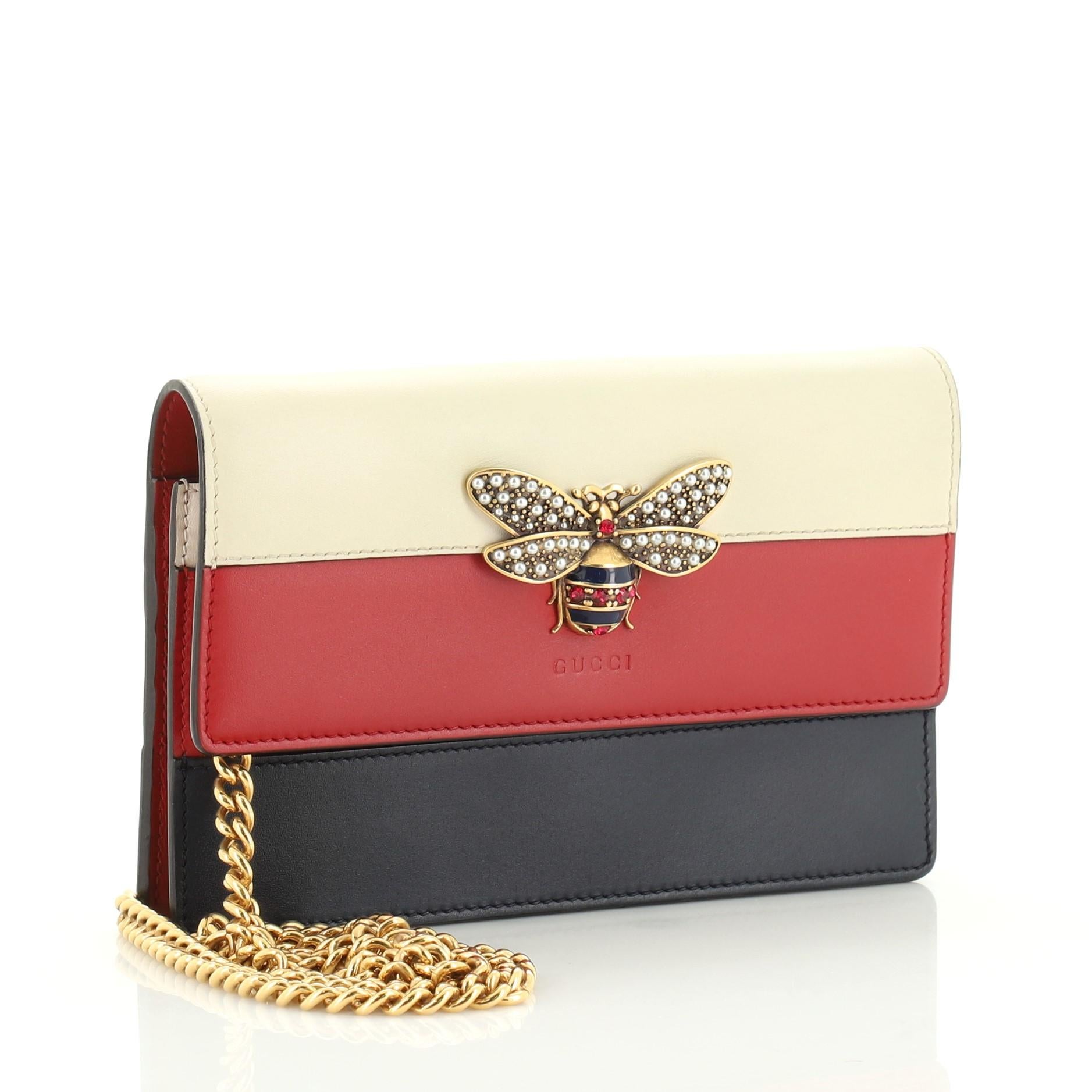 This Gucci Queen Margaret Chain Wallet Leather Mini, crafted from blue, red, and white leather, features a bejeweled bee on its flap, slip pocket under flap, and aged gold-tone hardware. Its snap button closure opens to a brown and red fabric and