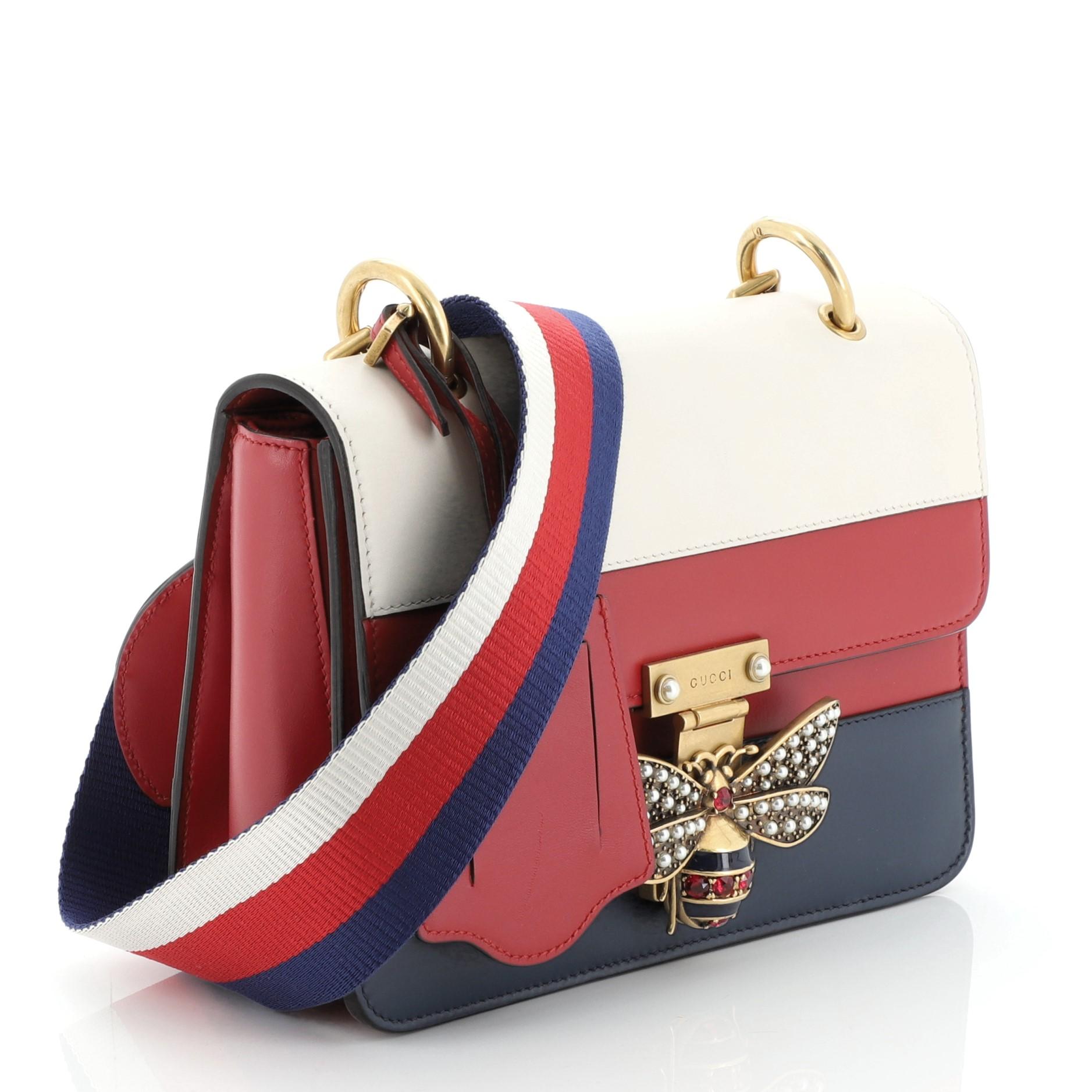 This Gucci Queen Margaret Flap Bag Colorblock Leather Medium, crafted from red, blue, white multicolor leather, features web shoulder strap, bejeweled bee on its flap, and aged gold-tone hardware. It opens to a neutral microfiber interior with side