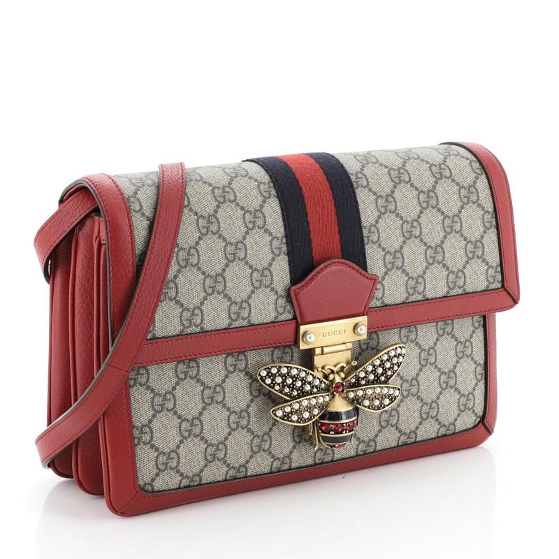 This Gucci Queen Margaret Shoulder Bag GG Coated Canvas Medium, crafted from neutral GG coated canvas, leather trim, features a leather shoulder strap, bejeweled bee as a symbol of wisdom and love on its flap, web strap and aged gold-tone hardware.