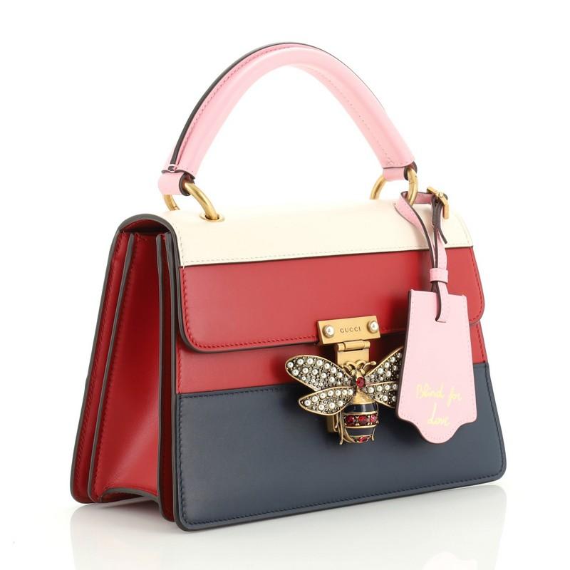 This Gucci Queen Margaret Top Handle Bag Colorblock Leather Small, crafted from multicolor, blue, pink, red, white leather, features a leather top handle, bejeweled bee on its flap, and aged gold-tone hardware. It opens to a neutral microfiber