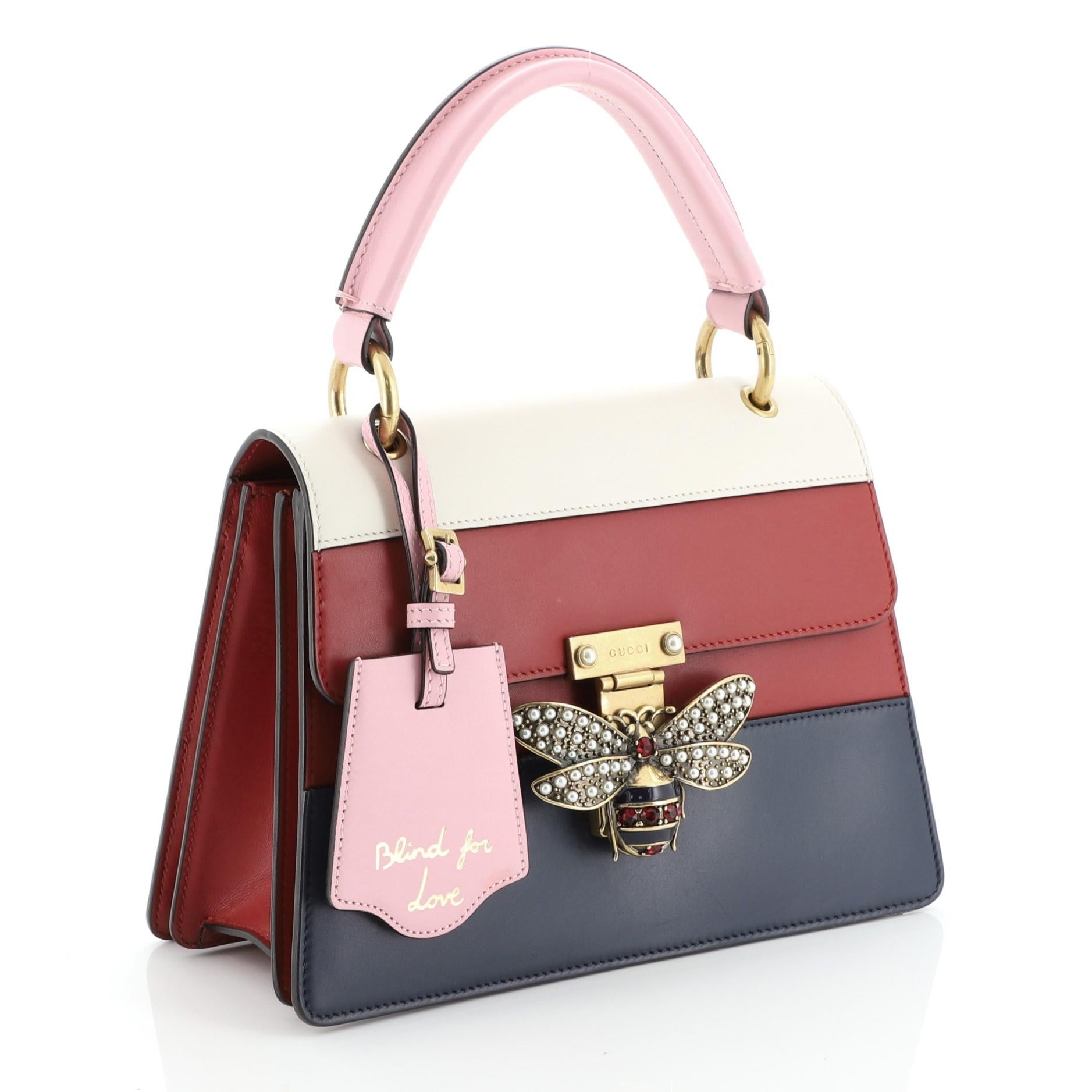 This Gucci Queen Margaret Top Handle Bag Colorblock Leather Small, crafted from blue, pink, red and white leather, features a leather top handle, bejeweled bee on its flap, and aged gold-tone hardware. It opens to a neutral microfiber interior