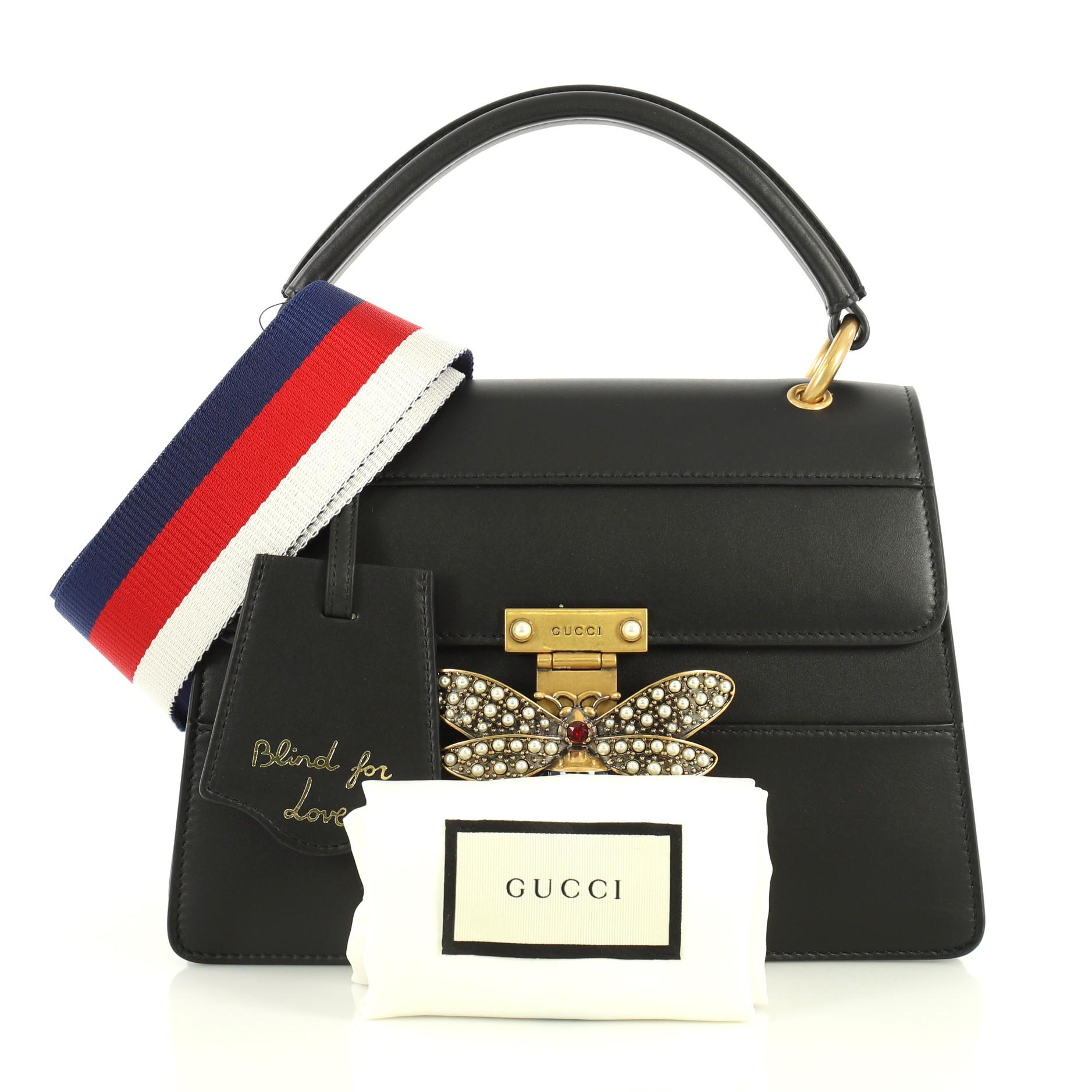 This Gucci Queen Margaret Top Handle Bag Leather Small, crafted from black leather, features a leather top handle, bejeweled bee on its flap, and aged gold-tone hardware. It opens to a neutral microfiber interior with three compartments and side
