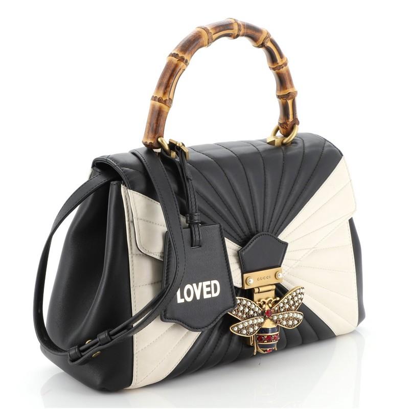 This Gucci Queen Margaret Top Handle Bag Quilted Leather Medium, crafted from black and white quilted leather, features a bamboo top handle, bejeweled bee on its flap, and aged gold-tone hardware. It opens to a neutral microfiber interior with side