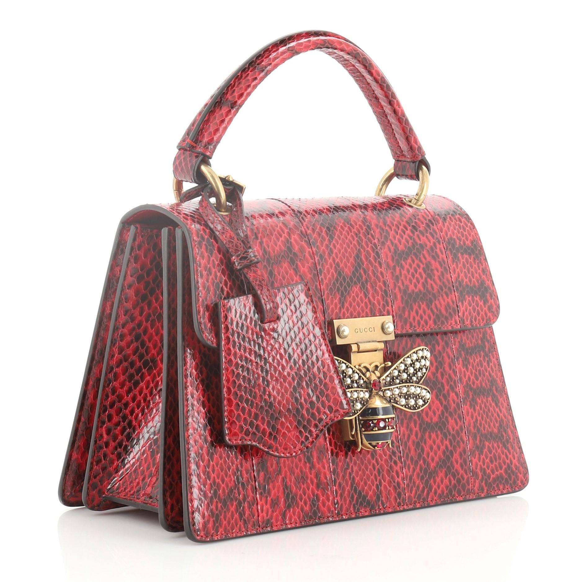 This Gucci Queen Margaret Top Handle Bag Snakeskin Small, crafted from genuine red snakeskin, features a leather top handle, bejeweled bee on its flap, and aged gold-tone hardware. It opens to a blue microfiber interior with three compartments and