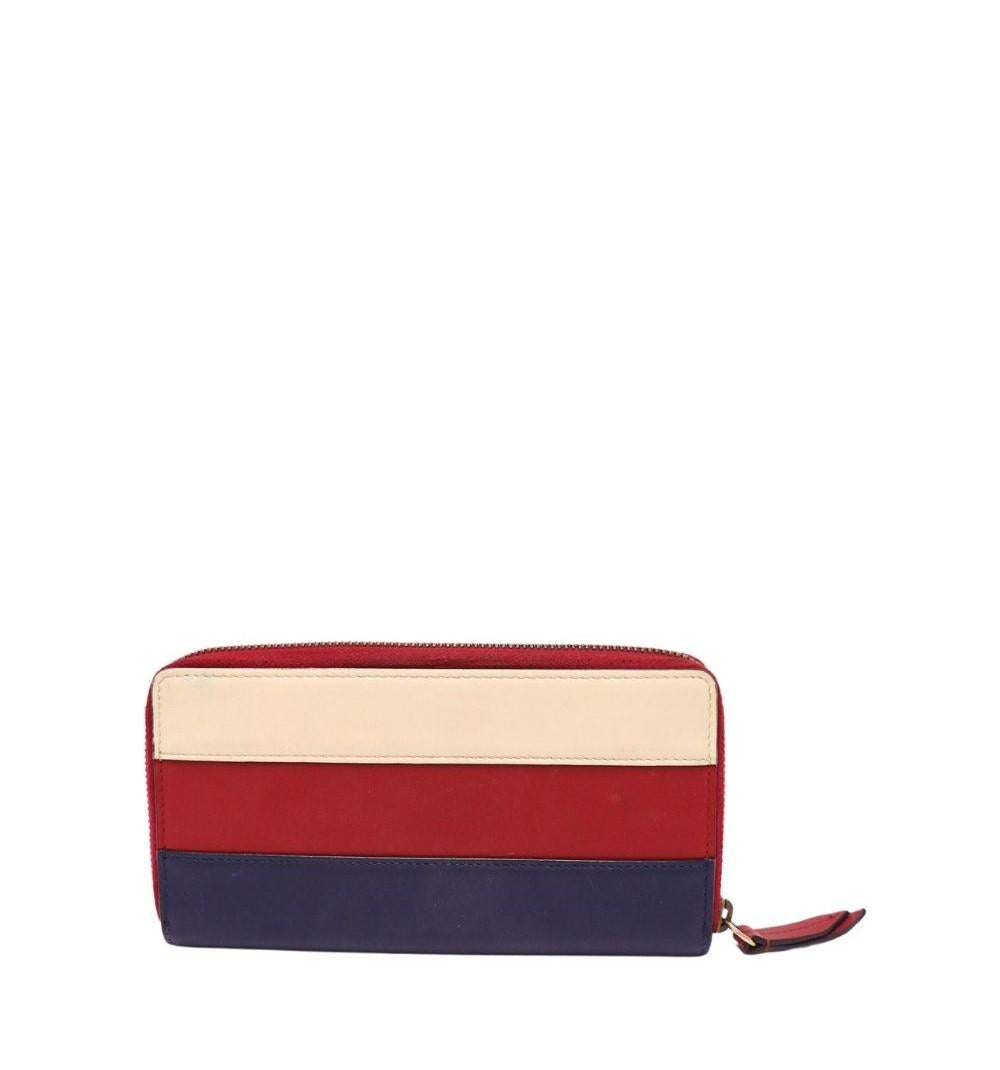 Add a touch of iconic luxury to your accessories collection with this Gucci tricolor leather wallet, featuring the house’s signature jeweled bee emblem. Crafted in rich red, white, and navy leather, this zip-around wallet combines timeless elegance