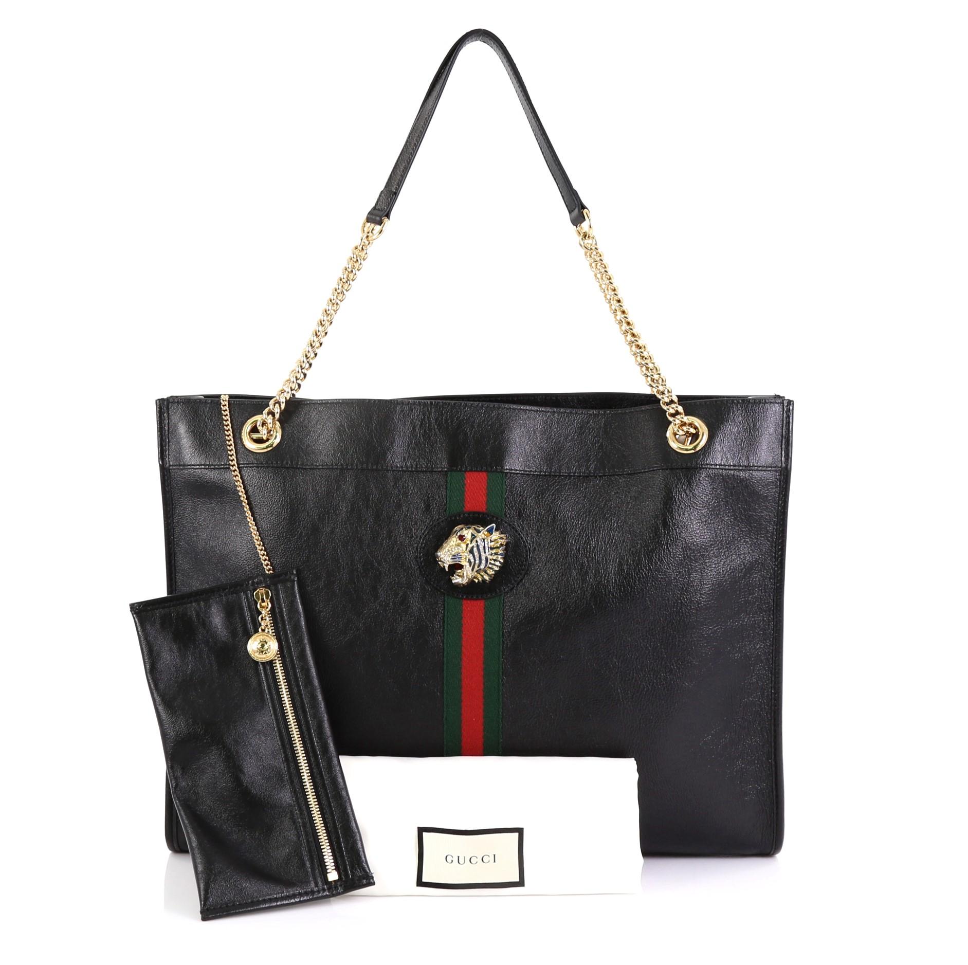 This Gucci Rajah Chain Tote Leather Large, crafted from black leather, features chain straps with leather pads, web stripe detailing, enameled tiger head with crystals, and gold-tone hardware. Its magnetic snap closure opens to a beige microfiber