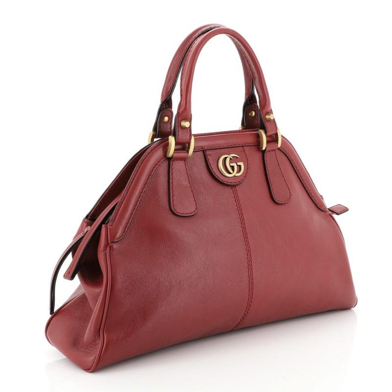 This Gucci RE(BELLE) Top Handle Bag Leather Medium, crafted from red leather, features dual rolled leather handles, framed top, GG interlocking logo, feline head details, and aged gold-tone hardware. Its top zip closure opens to a neutral microfiber