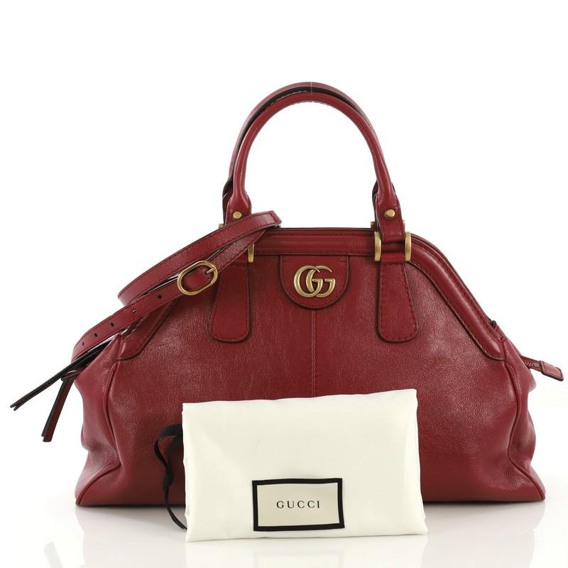 This Gucci RE(BELLE) Top Handle Bag Leather Medium, crafted from red leather, features dual rolled leather handles, framed top design, GG interlocking logo and feline head details, and aged gold-tone hardware. Its top zip closure opens to a beige