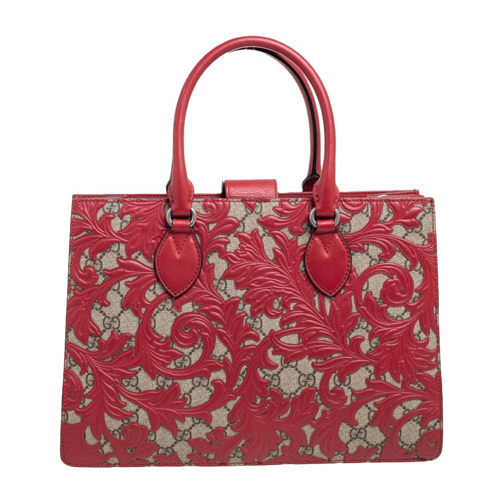 The intricate red leather detailing on the beige GG Supreme canvas body gives this Gucci Arabesque tote a unique and graceful appeal. Exquisitely crafted, the bag is complemented by gunmetal-tone hardware, double handles, an adjustable shoulder